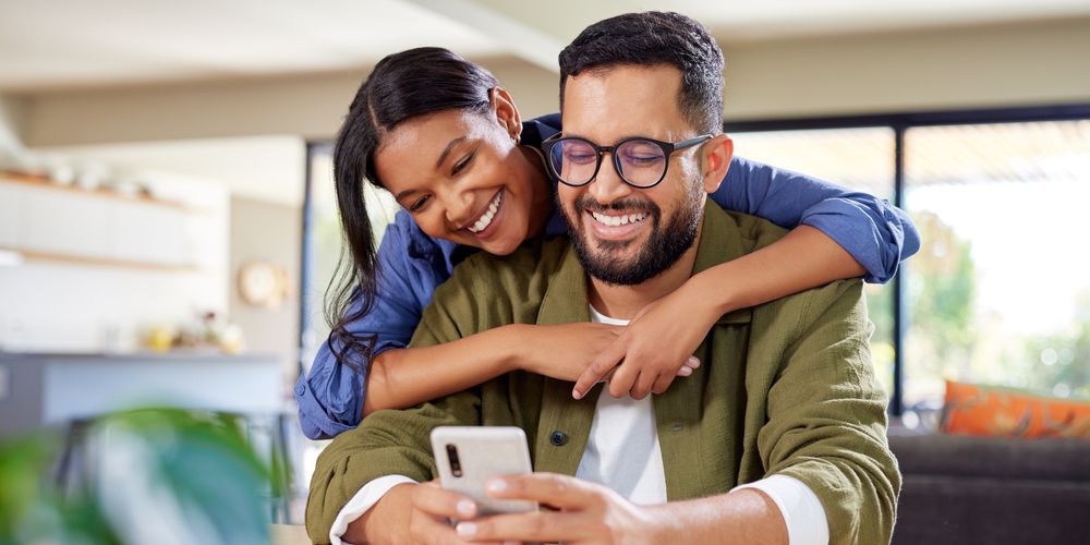 Woman smiling and hugging a man from behind.