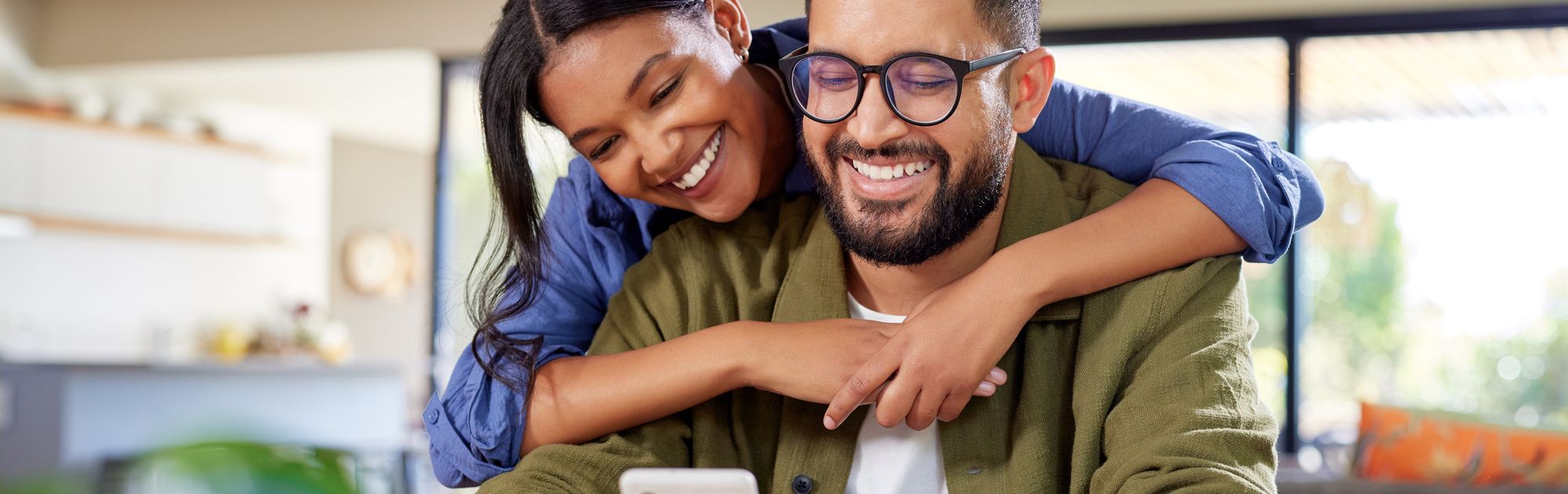 A woman playfully hugging the man from behind.