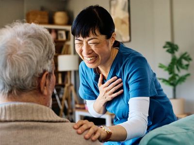 Healthcare worker in blue scrubs smiling and engaging an elderly person.