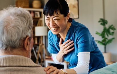 Caregiver smiling and comforting an elderly person on a couch.