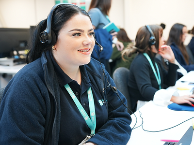 A woman with a headset smiles while working at a computer.