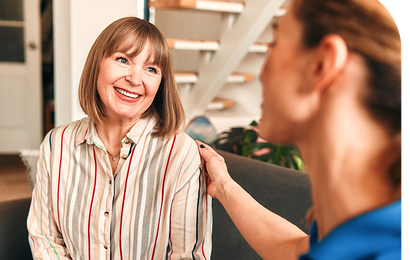 Two women sitting on a couch, smiling warmly at each other.