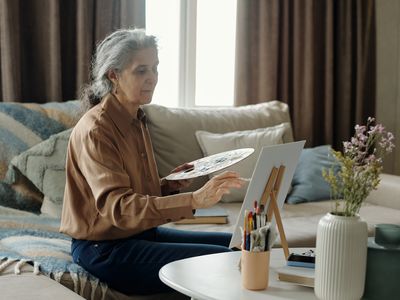 senior woman painting at living room table, on sofa
