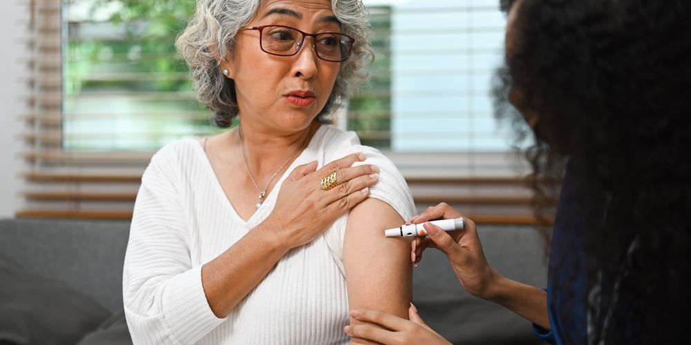 Close-up of a person lifting their sleeve while a nurse uses an injector pen to inject medication into the upper arm.