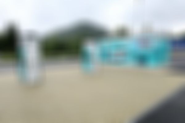 Elektrofahrzeug-Ladestation mit zwei Ladegeräten, einem Wandbild mit einem Auto und einem bewaldeten Hügel im Hintergrund unter bewölktem Himmel.