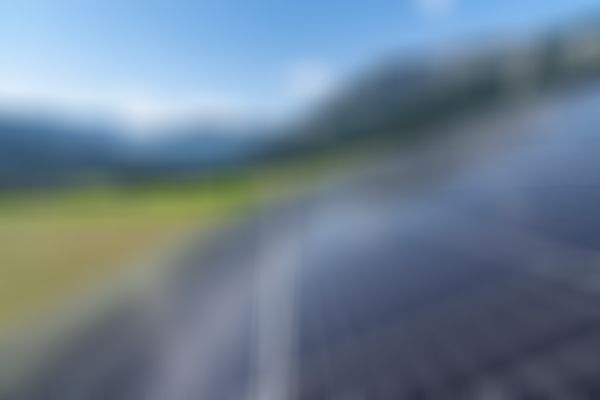 Sonnenkollektoren in einem grasbewachsenen Tal mit Bergen im Hintergrund unter einem strahlend blauen Himmel.