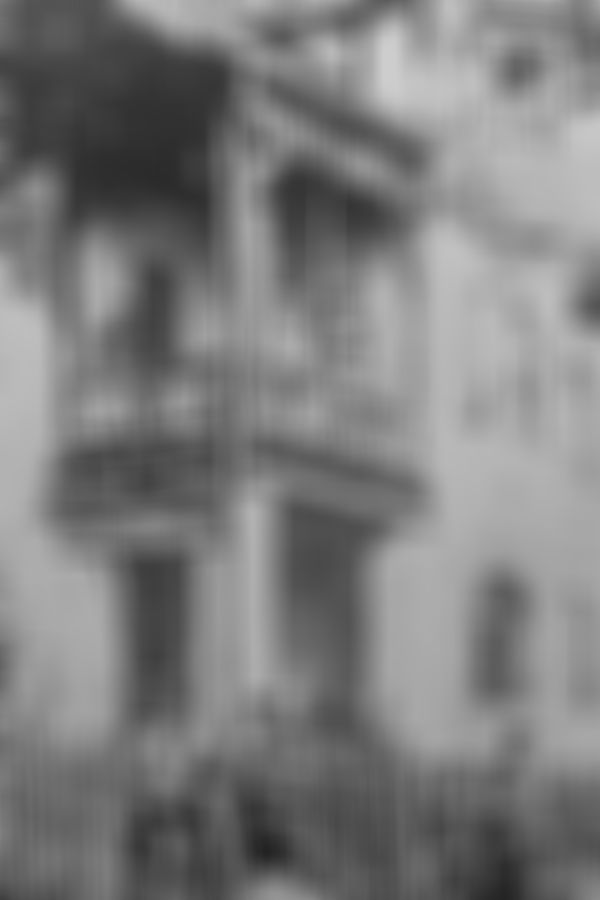 Historische Schwarz-Weiß-Aufnahme eines Gebäudes mit der Aufschrift „Bureau des Elektrizitätswerks“. Mehrere Personen stehen auf den Balkonen und vor dem Gebäude, zwei Männer sind mit Fahrrädern zu sehen.