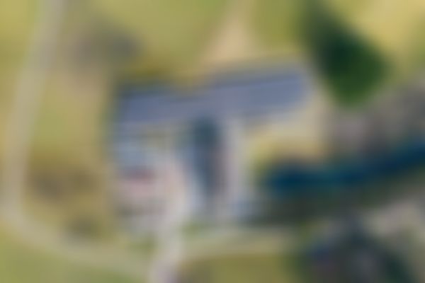 Luftaufnahme eines Solarkraftwerks mit zahlreichen Sonnenkollektoren, umgeben von Wiesen, Bäumen und einem kleinen Wasserspeicher.