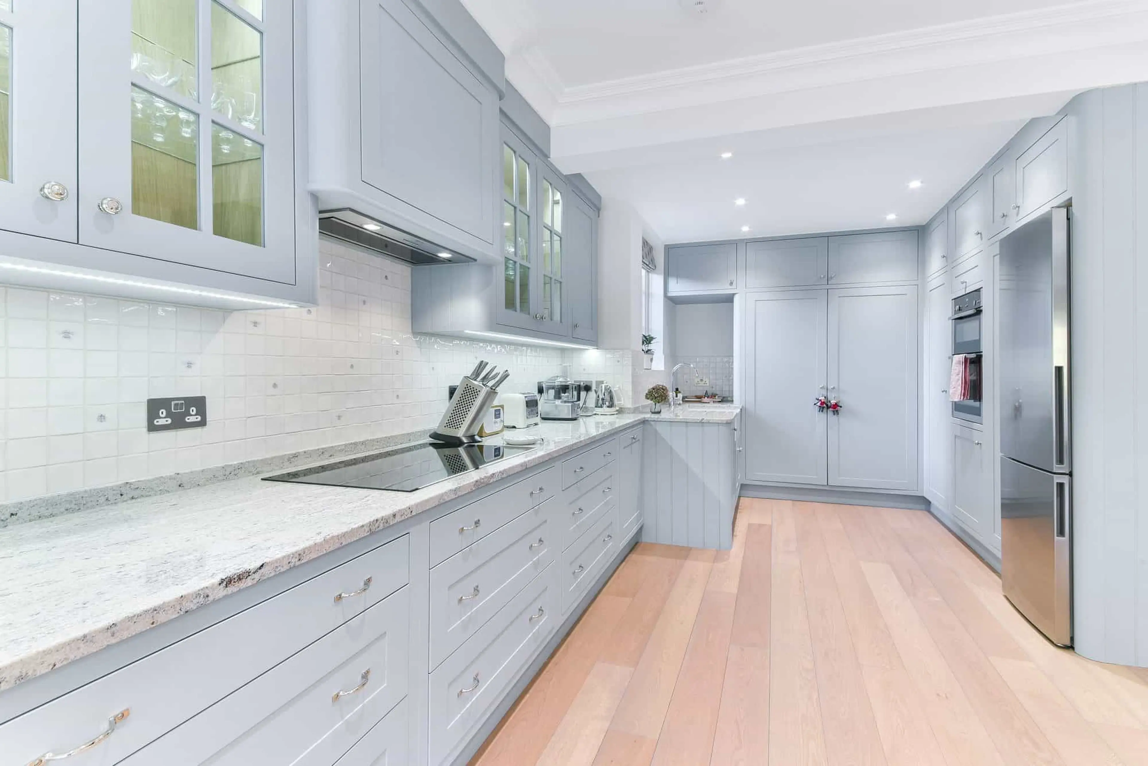 Kitchen run with stone worktop, glazed wall cabinets and integrated appliances