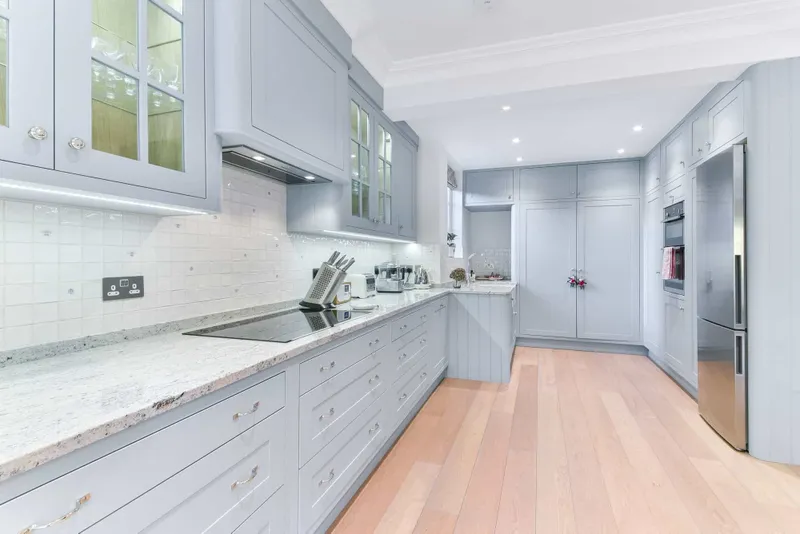 Kitchen run with stone worktop, glazed wall cabinets and integrated appliances