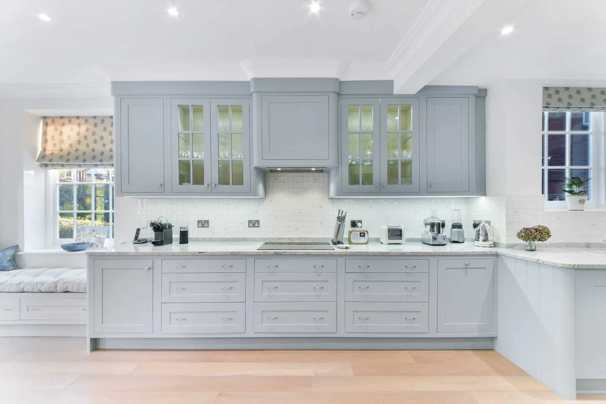 Bespoke kitchen with pale blue-grey shaker units, stone worktops and glazed wall cabinets