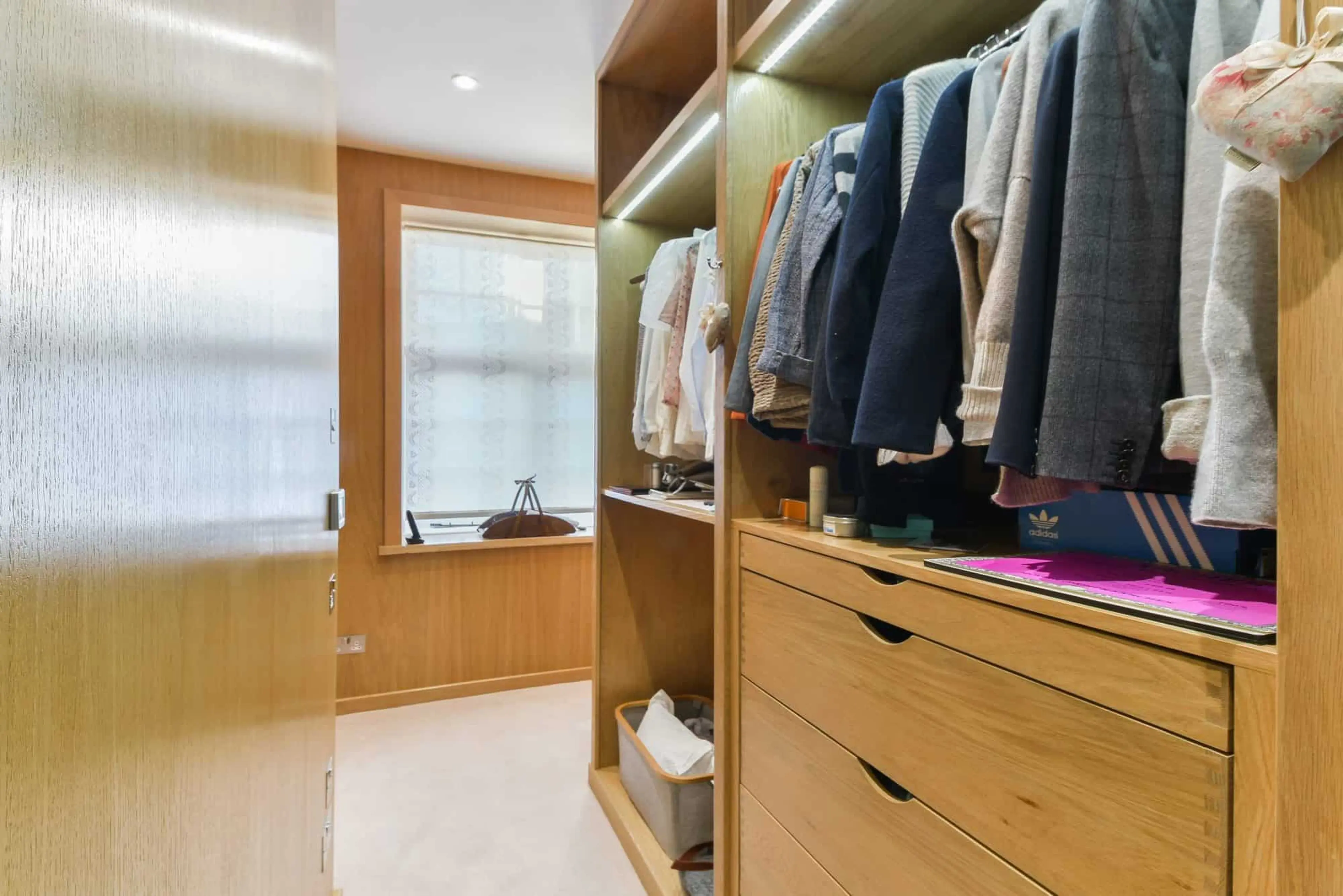 Walk-in wardrobe lined in oak veneer with LED lighting