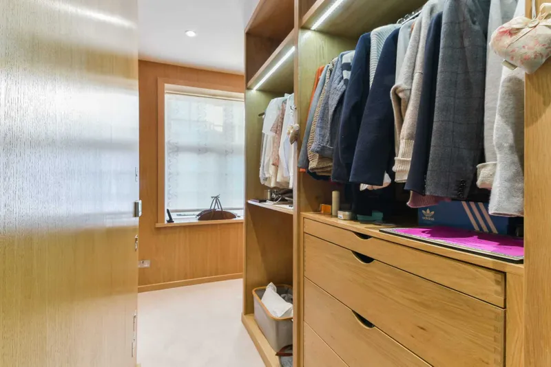Walk-in wardrobe lined in oak veneer with LED lighting