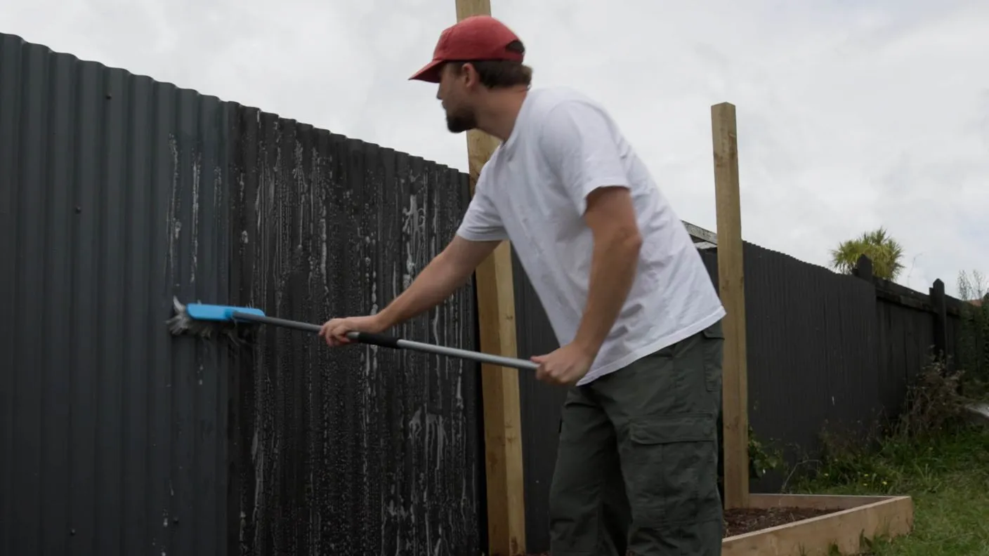 Cleaning Colorbond fence with broom and suds to clean dirt and grime