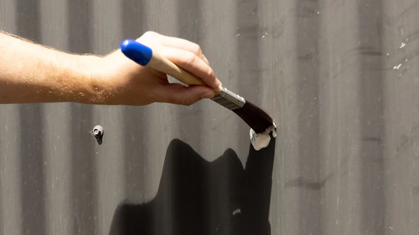 Person applying Rust Guard Rust Converter to corrugated fence