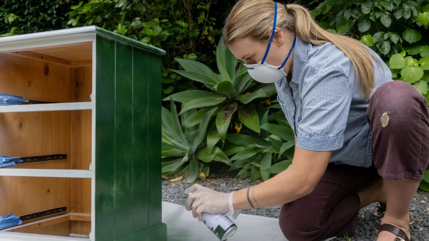 Woman spray painting chest of drawers with White Knight Squirts in a green colour outdoors