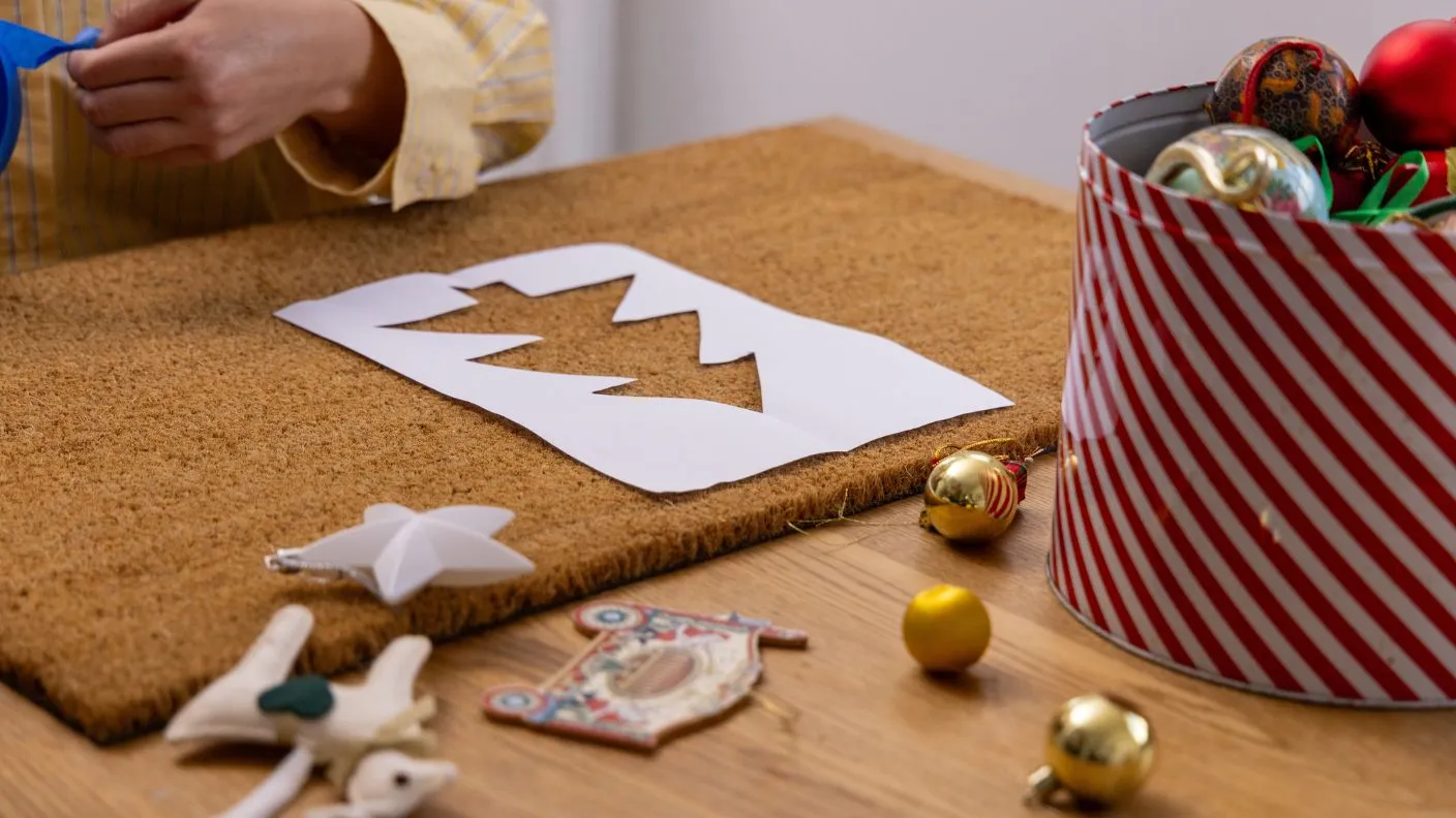 Christmas tree stencil cut out and placed upon door mat with other decorations around