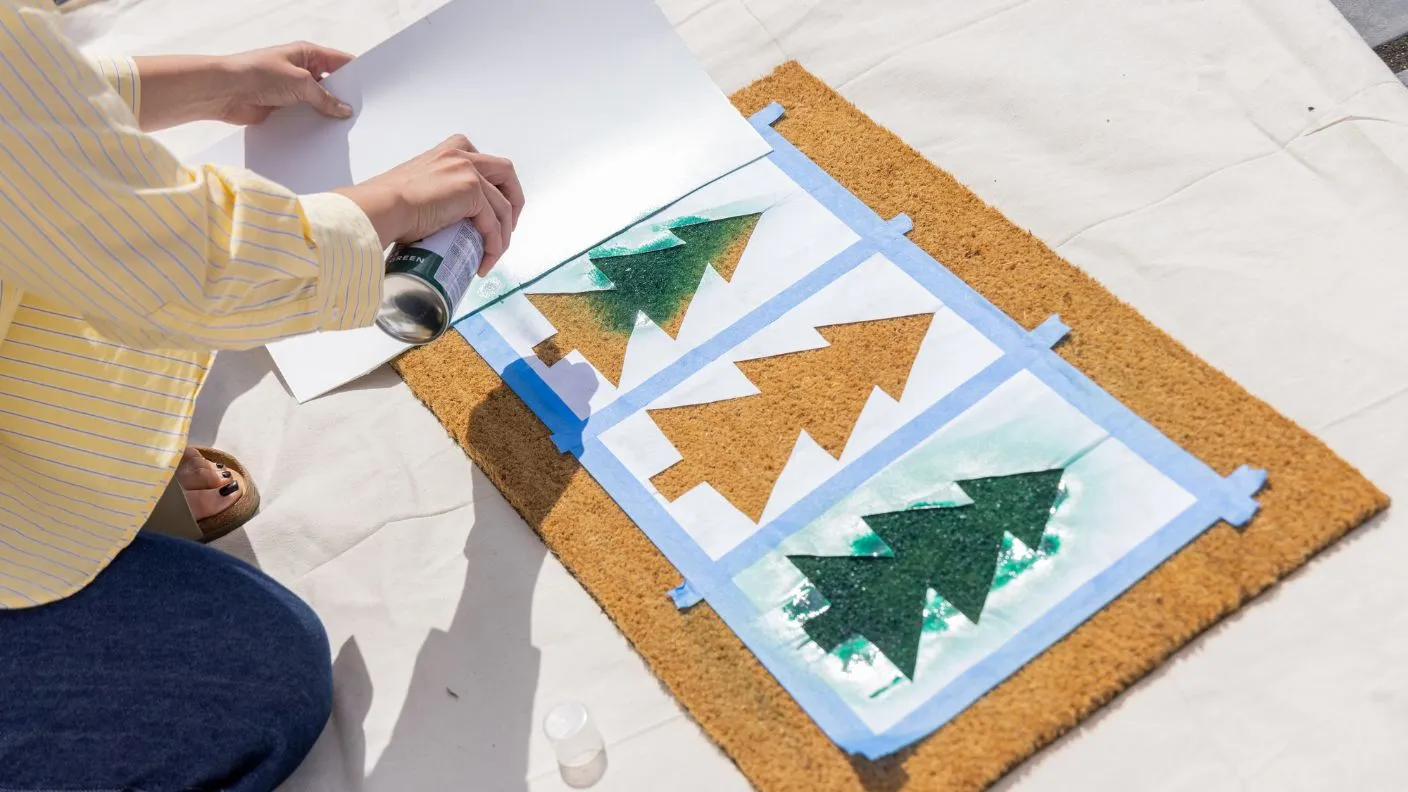 White Knight Squirts being sprayed onto stencils to create green trees on festive themed door mat