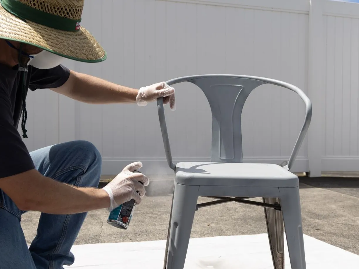 Spraying White Knight Rust Guard all-purpose primer in grey onto a metal outdoor chair