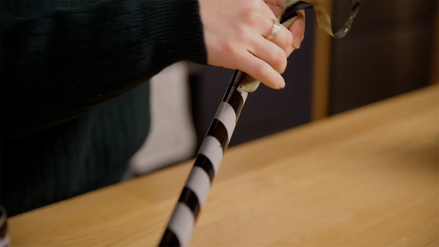 Hands wrapping a striped gift with ribbon on a wooden table.