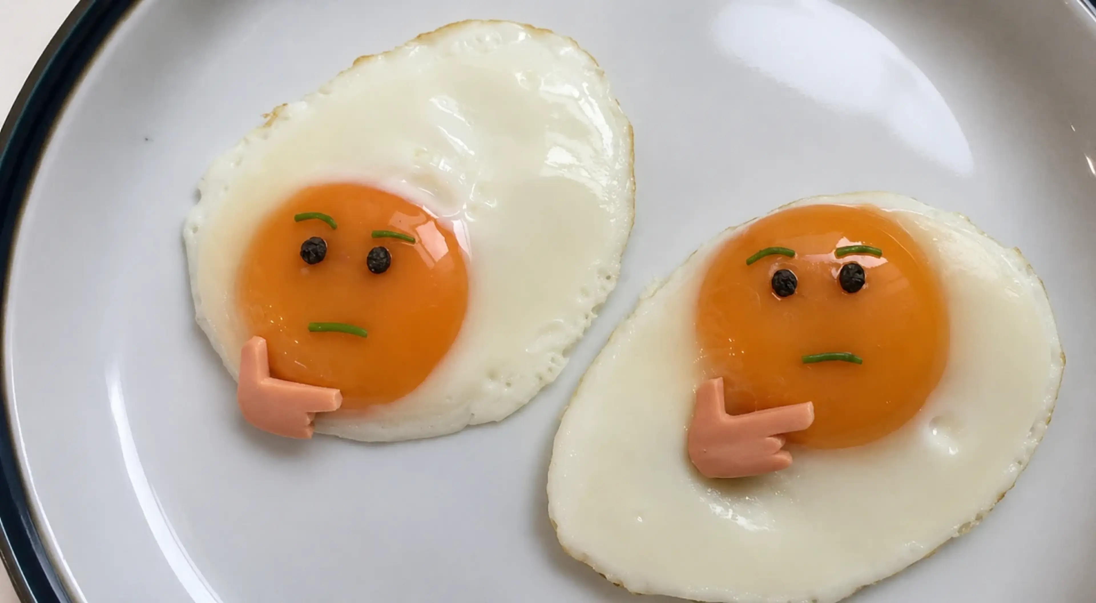 Two fried eggs decorated with tiny faces and hands in a thinking pose on a white plate, creatively illustrating the concept of critical thinking