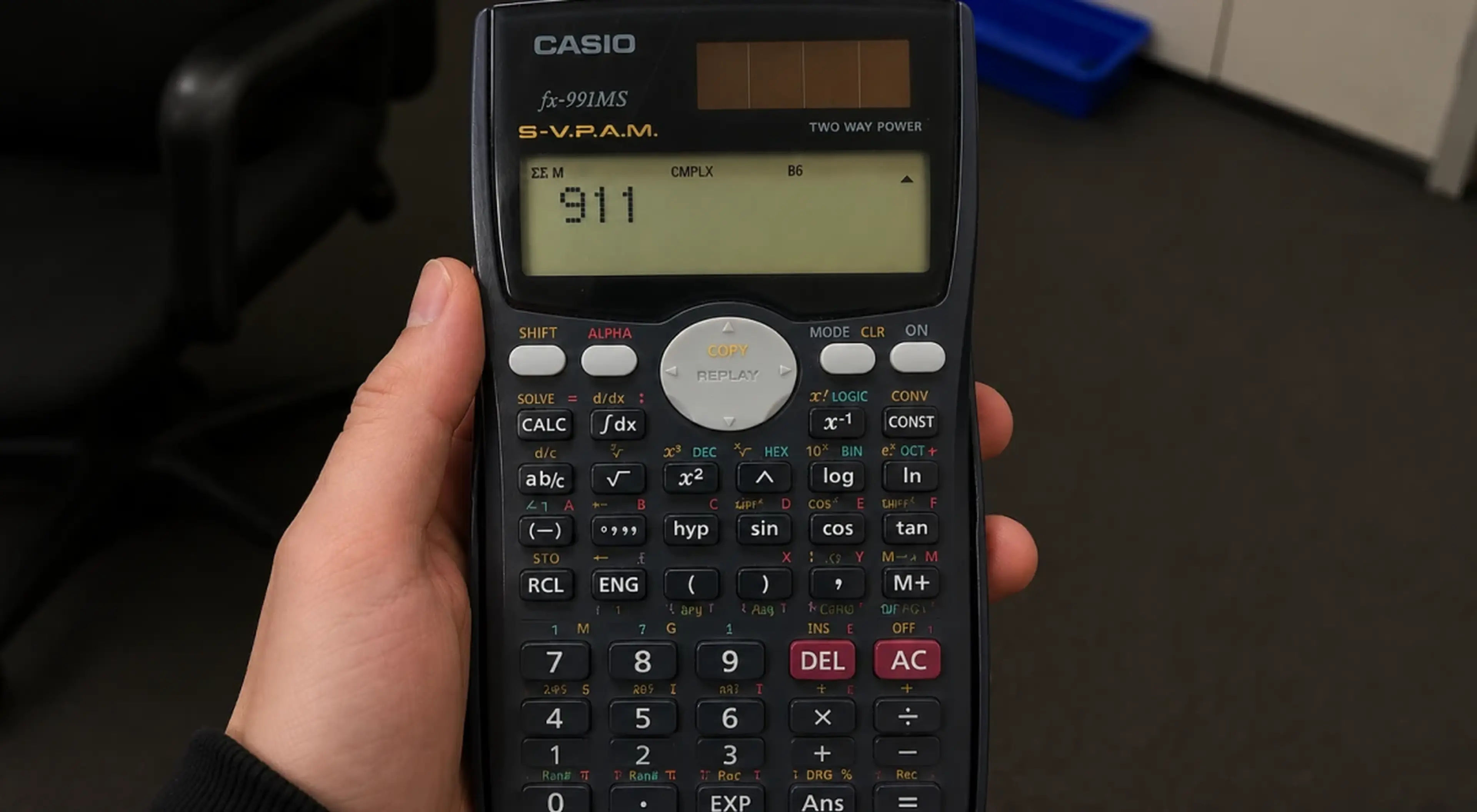 Hand holding a Casio fx-991MS scientific calculator displaying 911 on the screen, set against a dark desk background illustrating the counting principle in real life