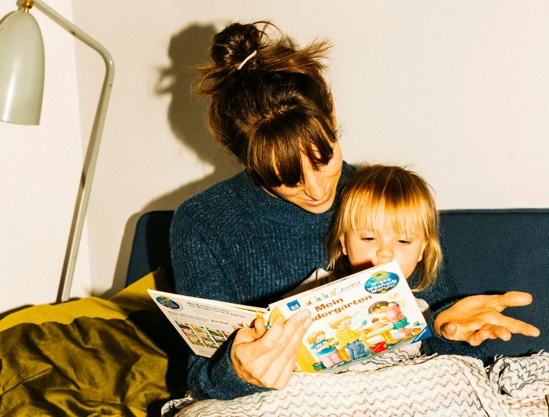 Mutter sitzt auf dem Sofa und liest ihrer Tochter ein Buch vor.