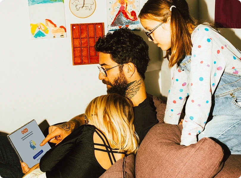 Vater sitzt mit seinen zwei Töchtern auf dem Sofa, alle schauen gemeinsam auf ein iPad mit dem hiToco-Startbildschirm.