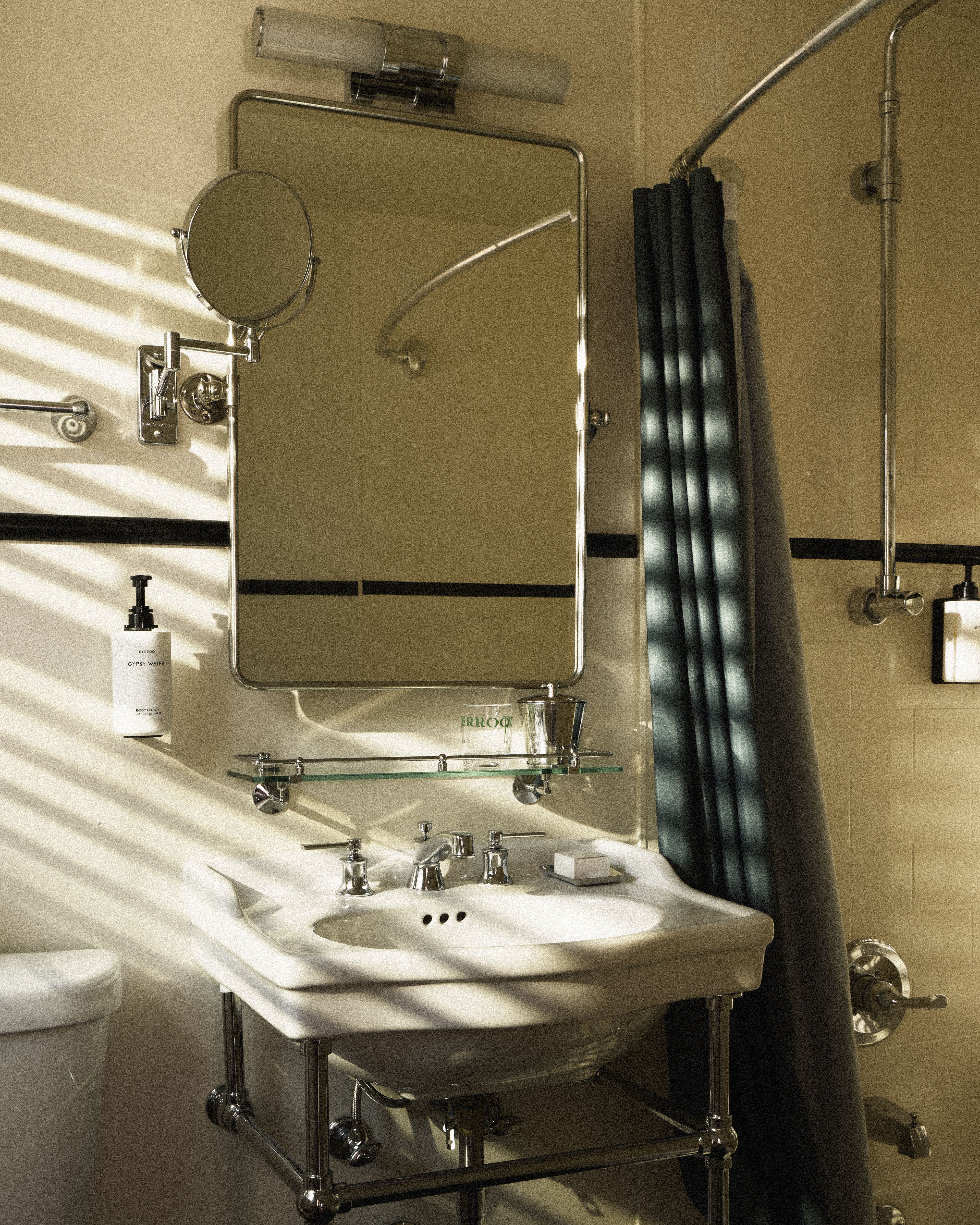 Bright guest bathroom with vintage-style pedestal sink, chrome fixtures, walk-in shower, and Byredo amenities at Perroquet Hotel.