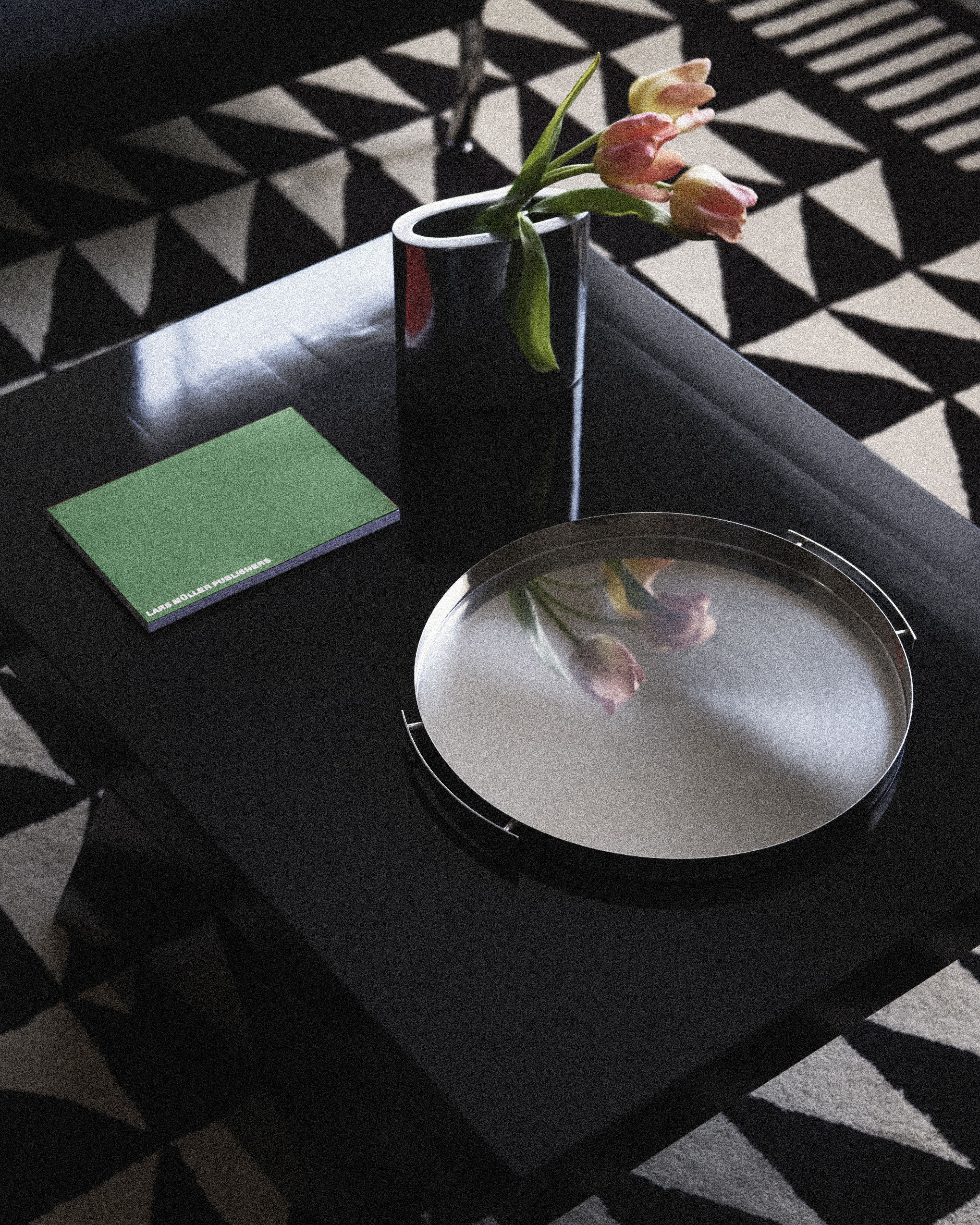 Modern coffee table with fresh tulips, design books, and reflective tray at Perroquet Hotel.