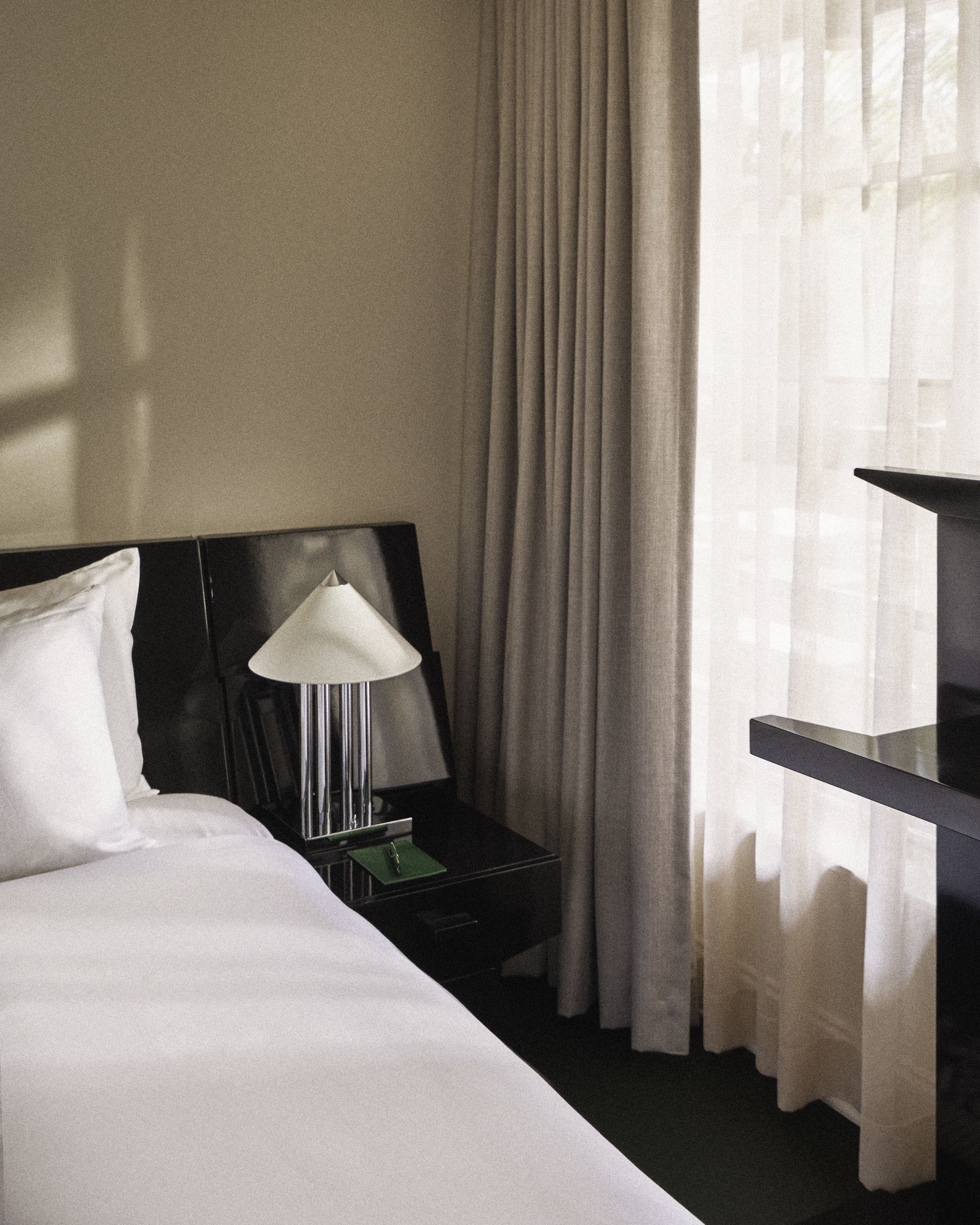 Modern bedside lamp and nightstand beside a king bed in a thoughtfully designed Perroquet Hotel guest room.