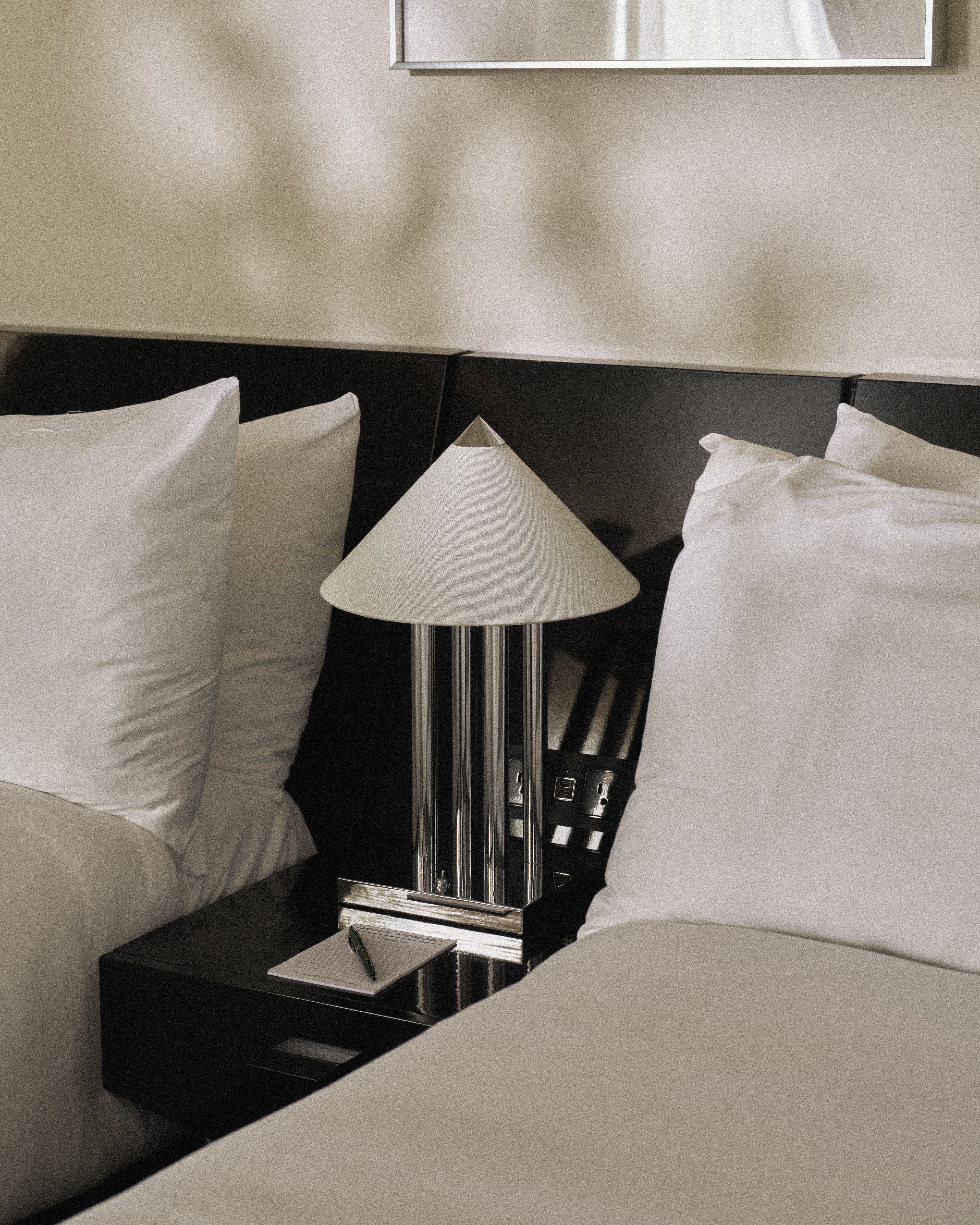 Designer bedside table with sculptural lamp between two queen beds at Perroquet Hotel.