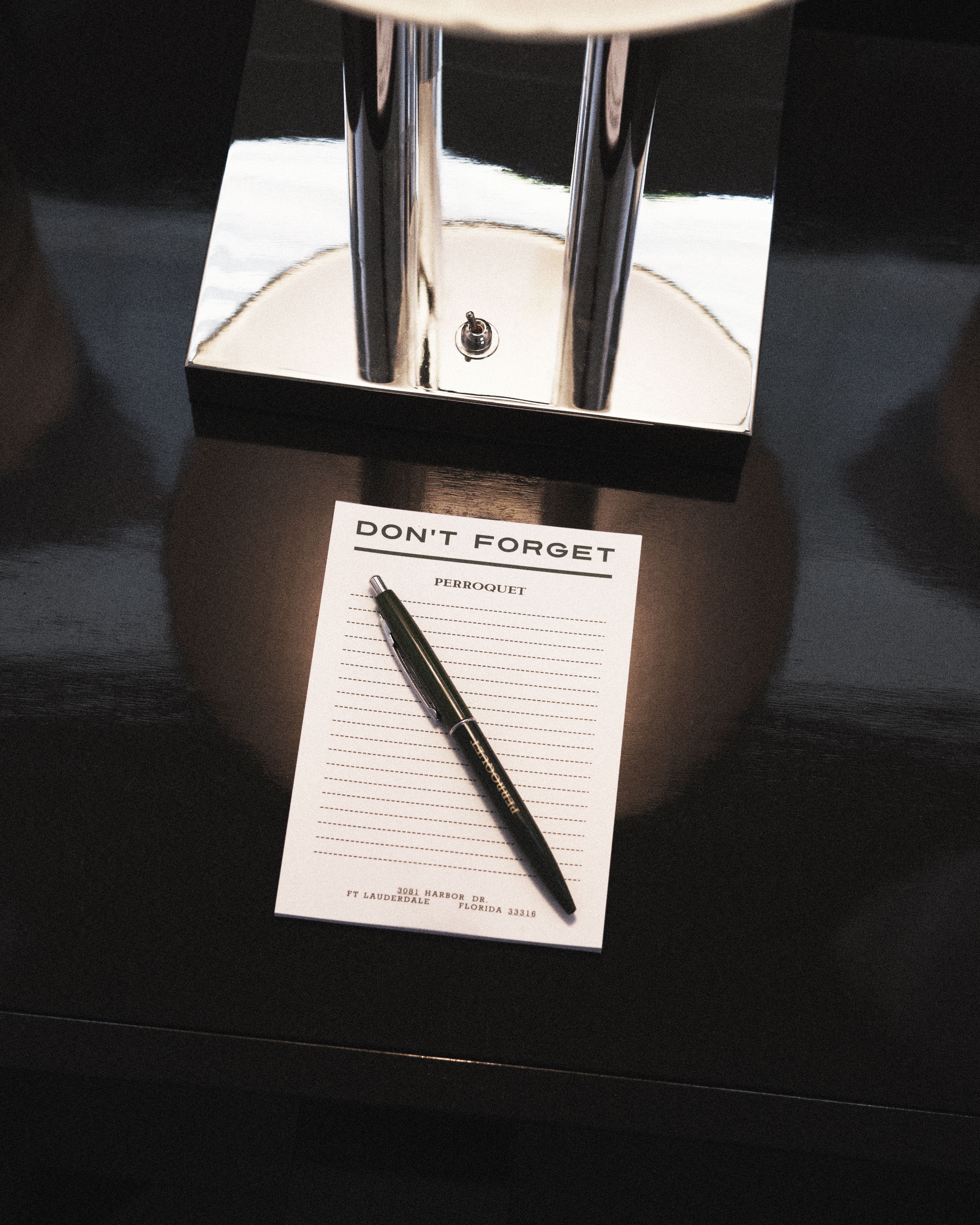 Perroquet Hotel branded notepad and pen on a sleek black bedside table beneath a contemporary lamp.