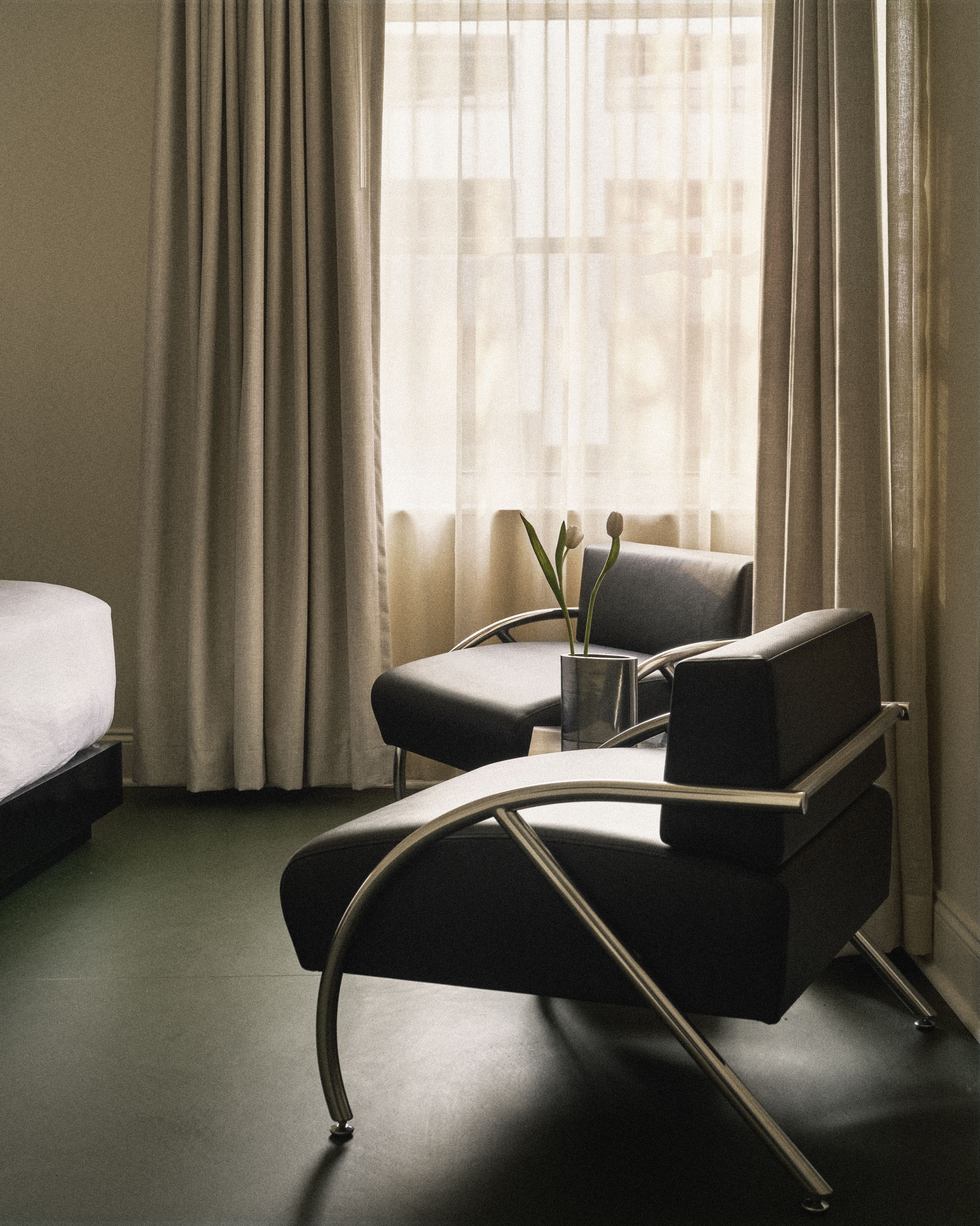 Modern lounge chairs beside a sunlit window create a quiet reading corner in a Perroquet Hotel guest room.