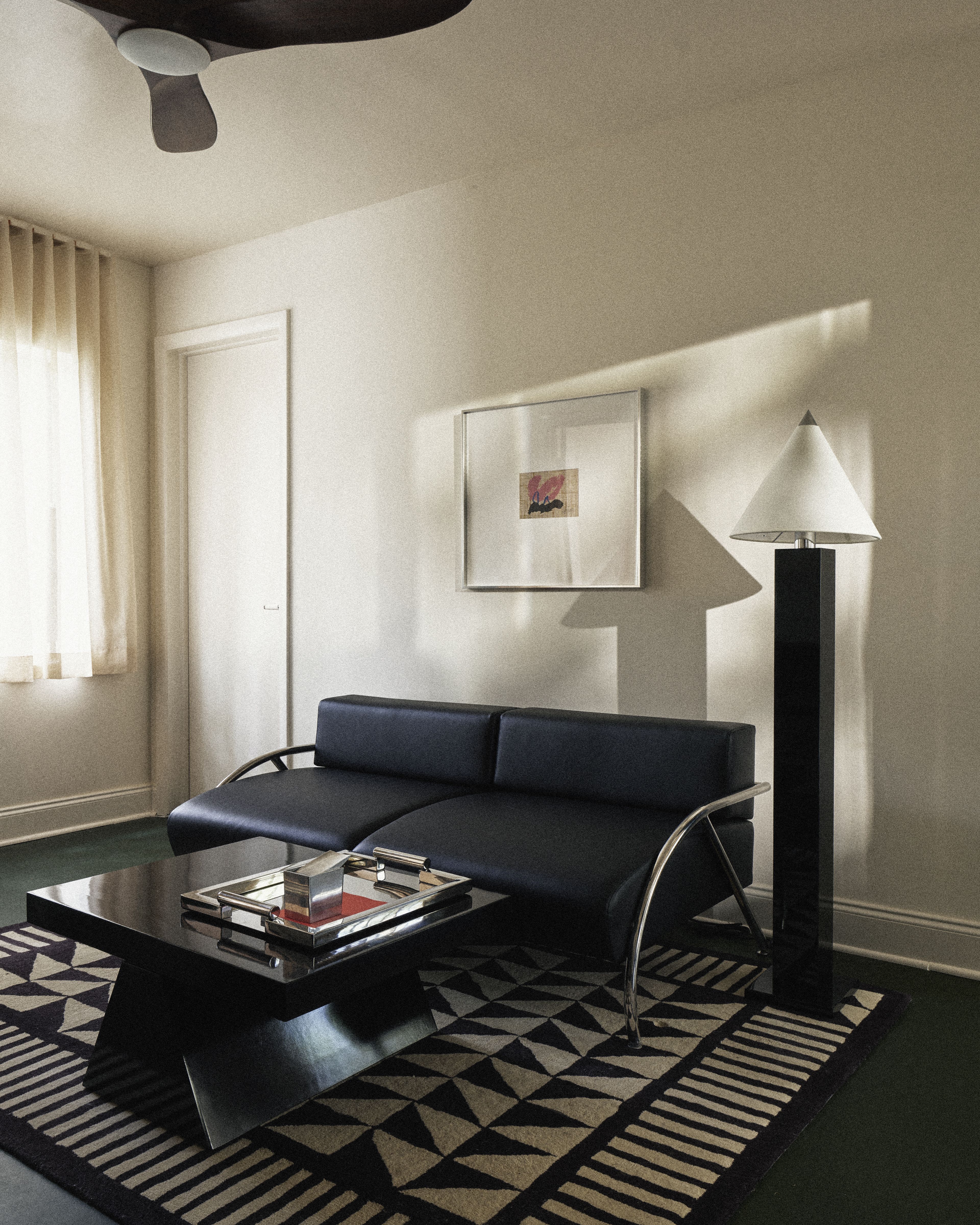 Modern guest room living area with black leather sofa, sculptural coffee table, and designer floor lamp.