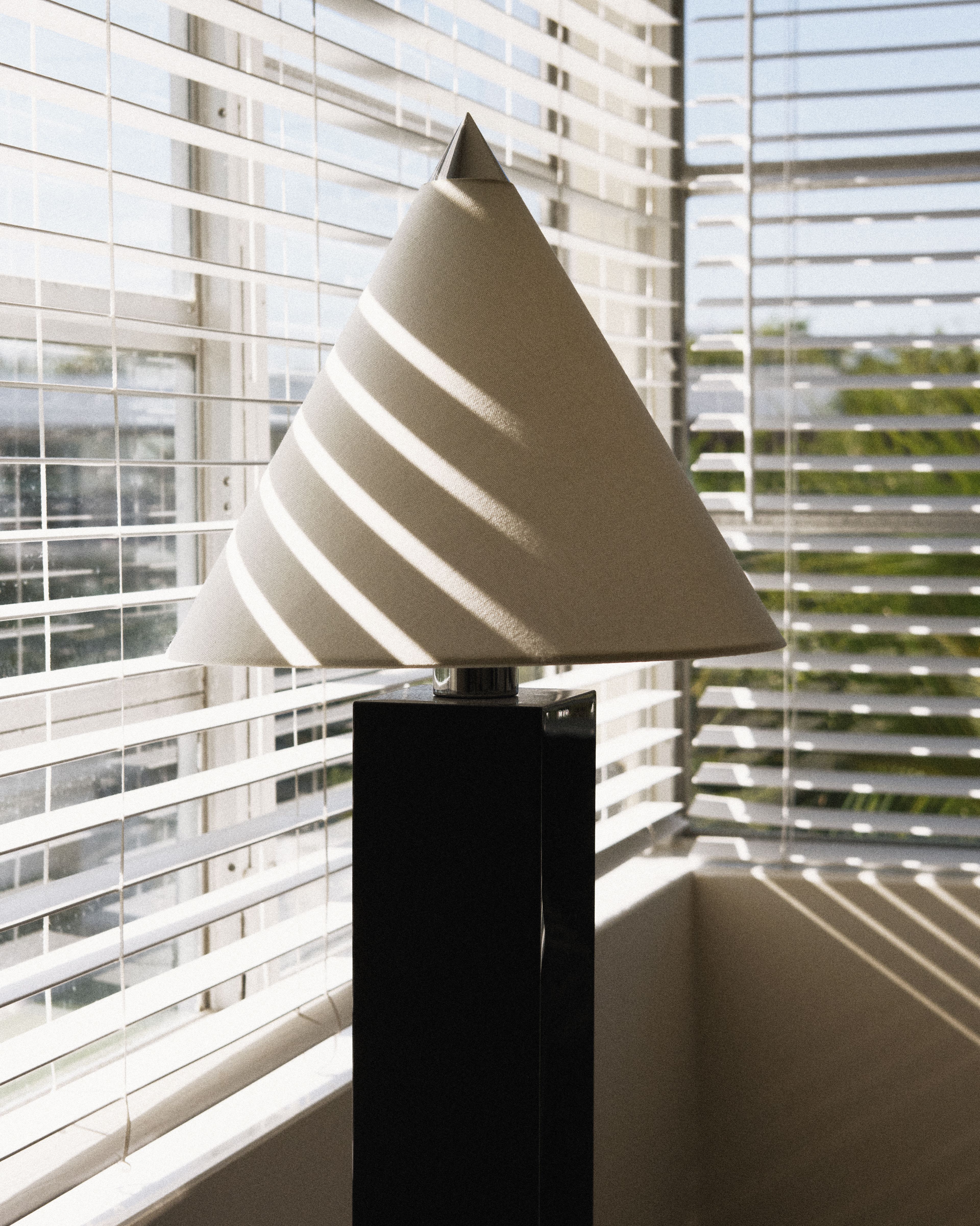 Contemporary bedside lamp beside a sunlit window with plantation shutters in a guest room at Perroquet Hotel.