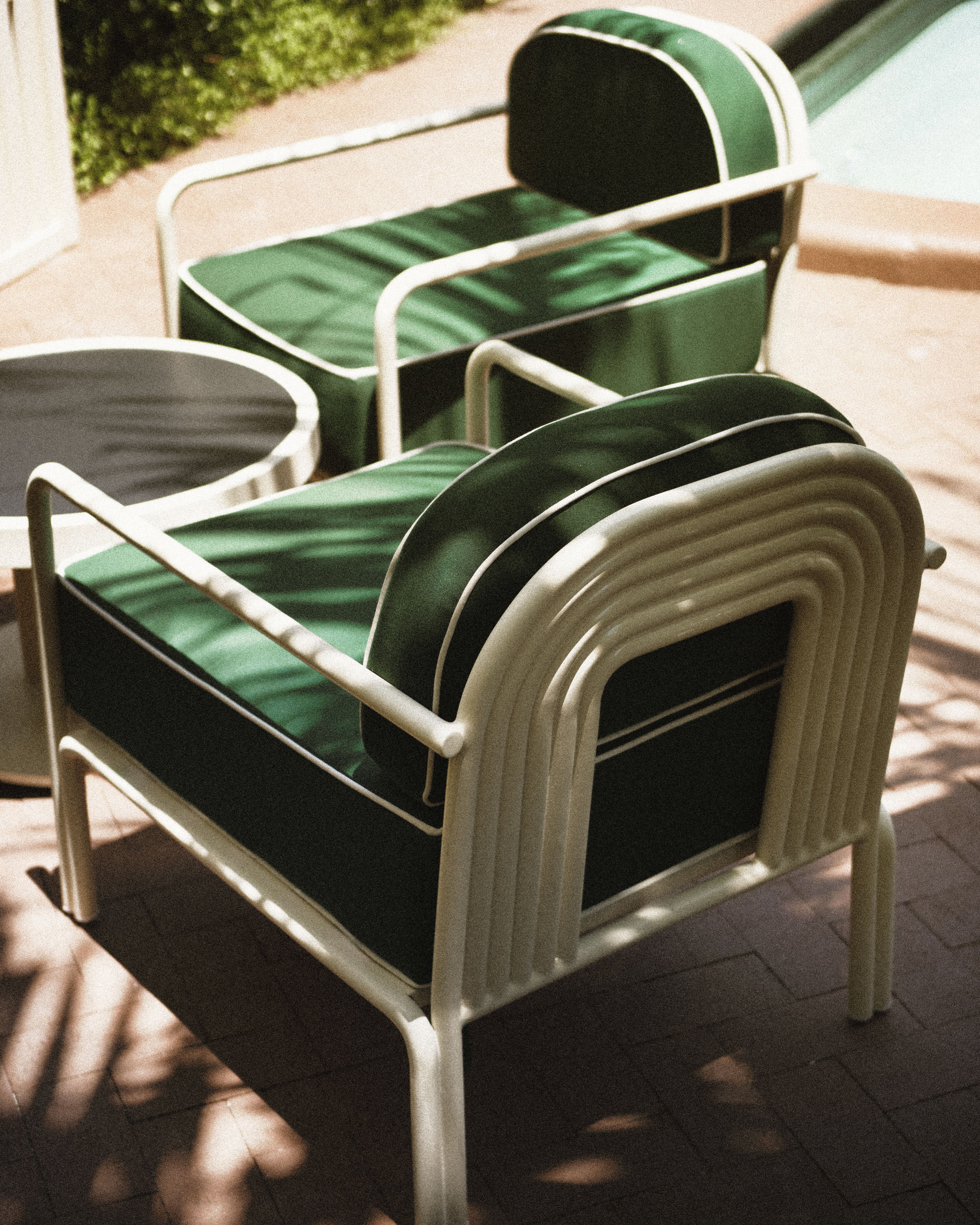 Green cushioned poolside lounge chairs with white frames beside the swimming pool at Perroquet Hotel.