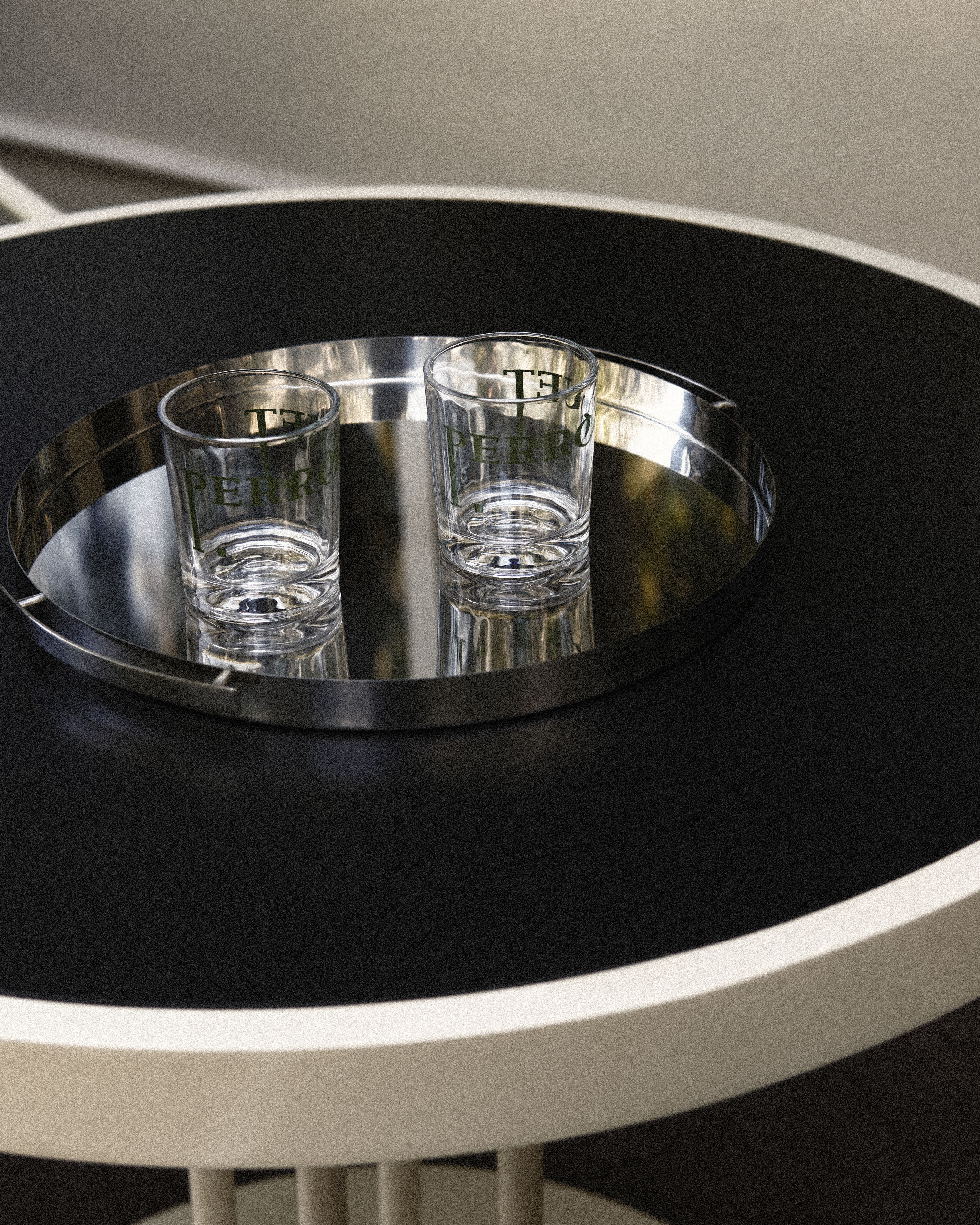 Two Perroquet Hotel branded drinking glasses displayed on a polished serving tray atop a modern side table.