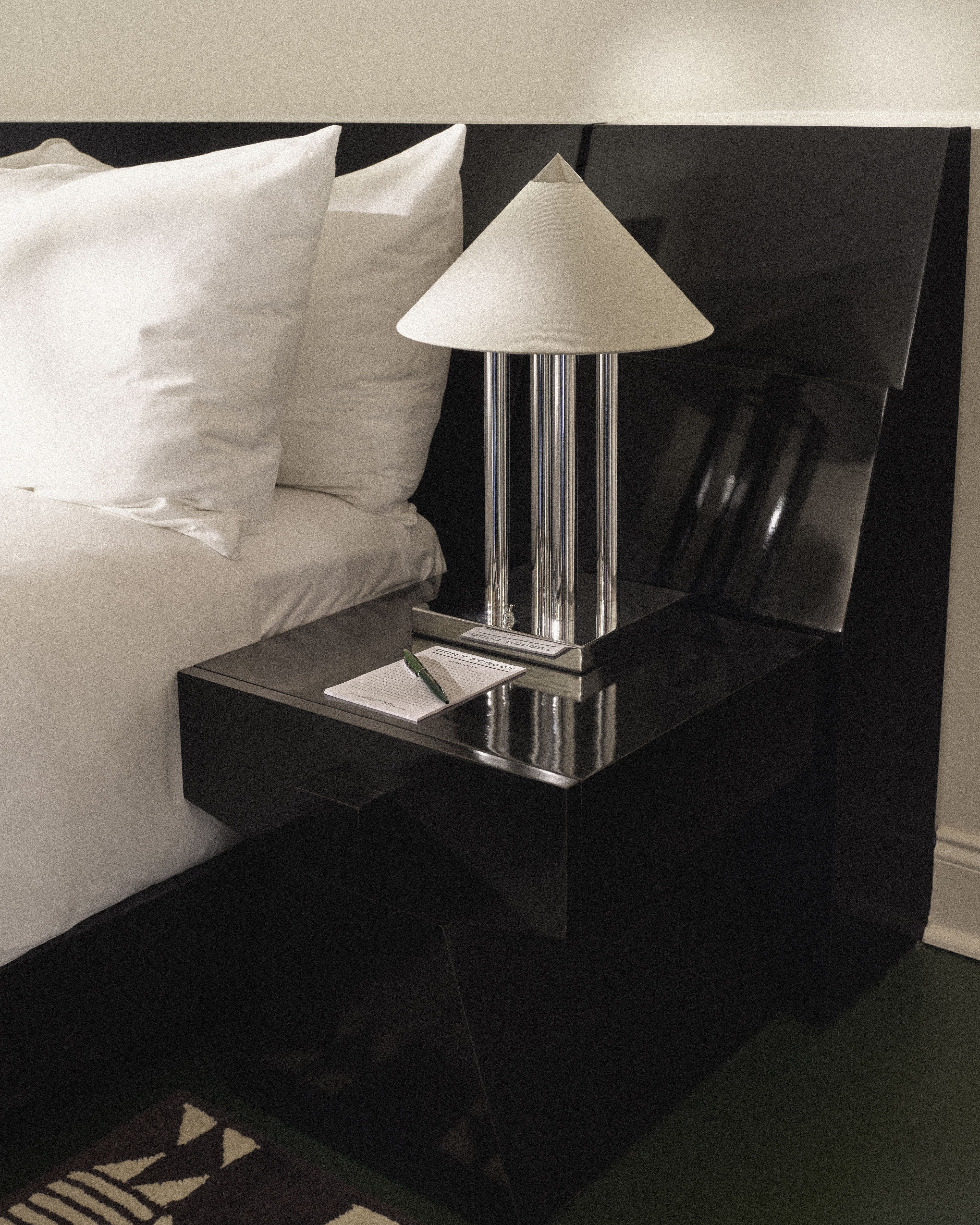 Contemporary bedside lamp and nightstand with notepad in a Perroquet Hotel guest room.