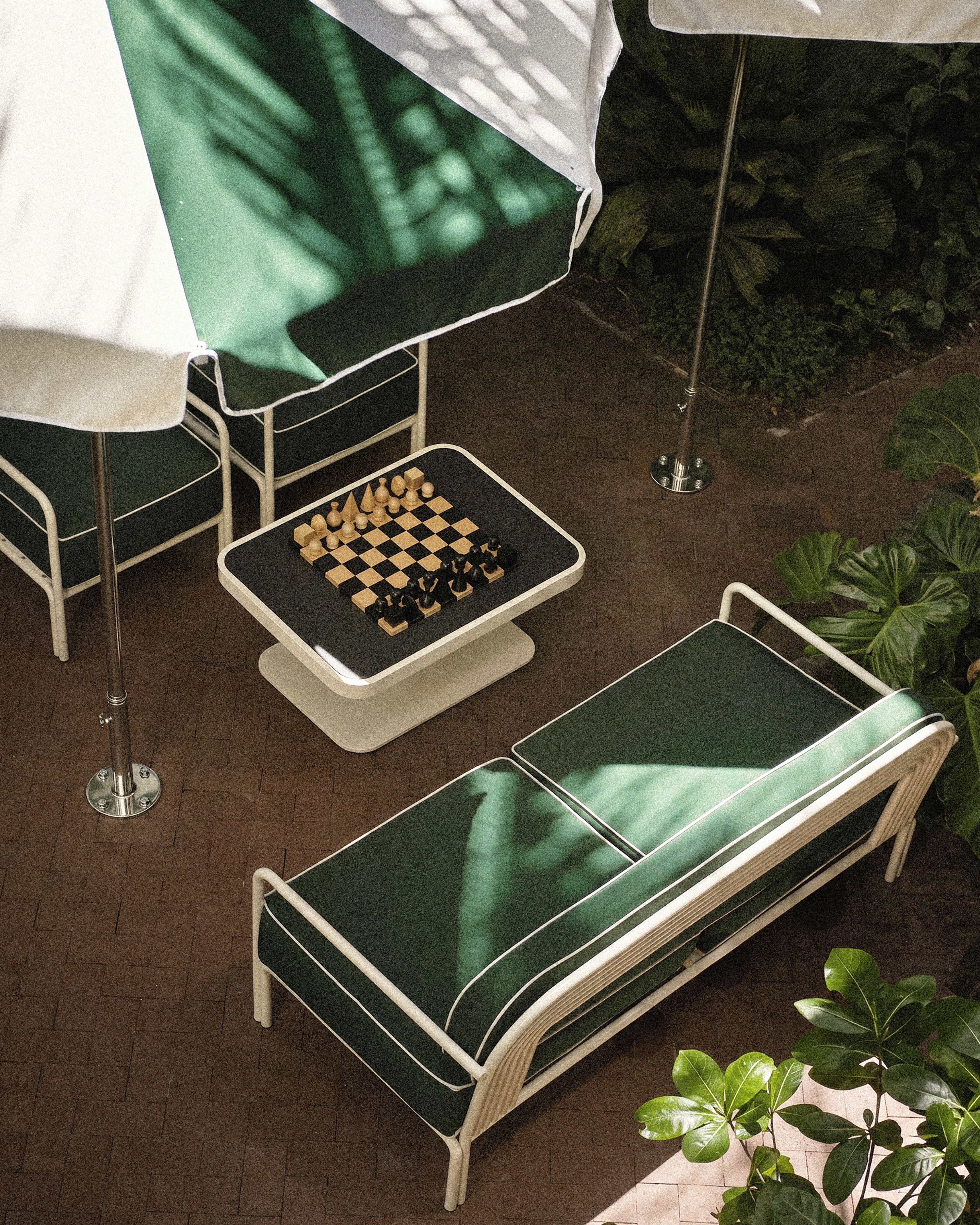Outdoor lounge area with green seating, oversized chess set, and tropical landscaping at Perroquet Hotel.