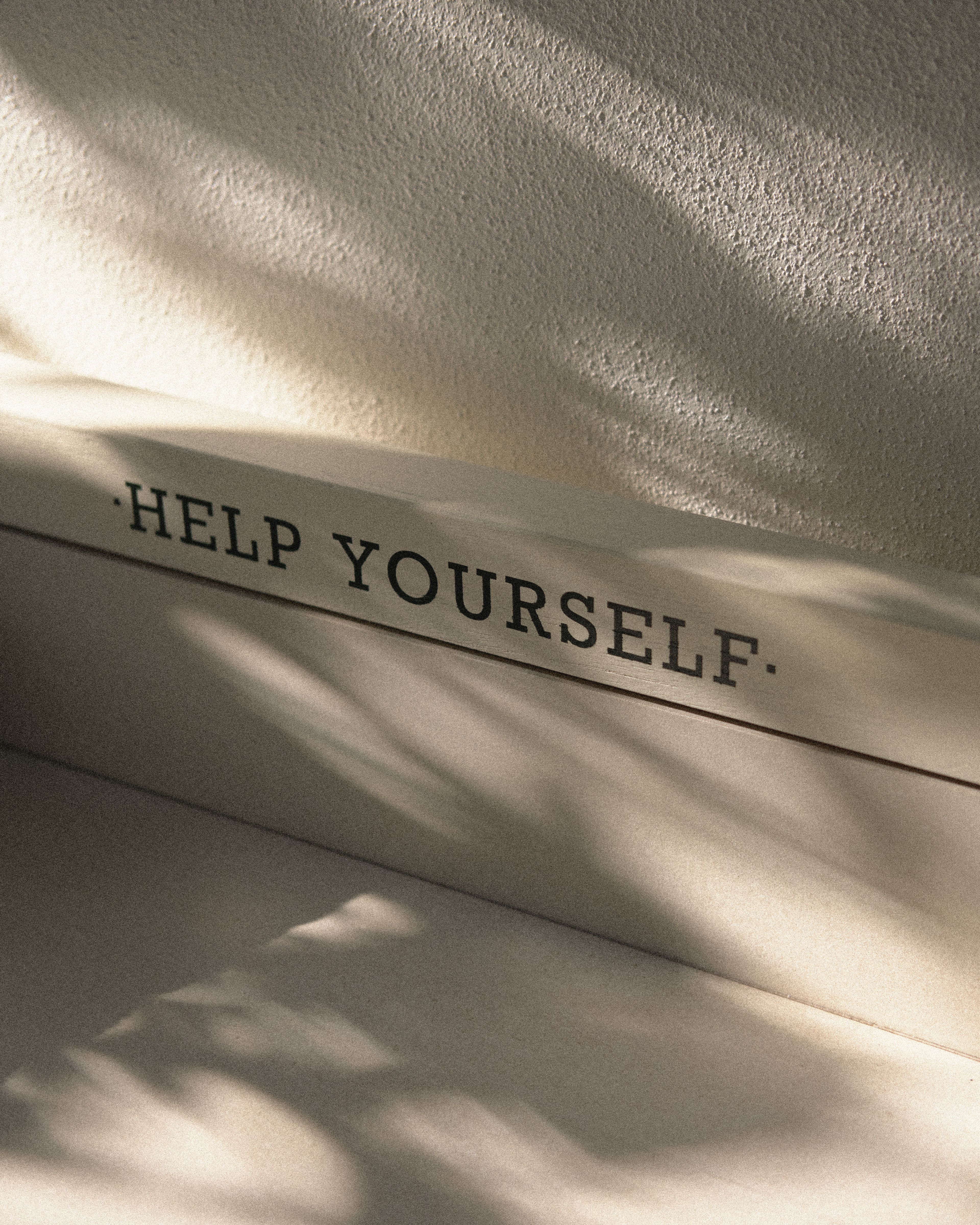 "Help Yourself" hospitality station sign illuminated by natural light and tropical palm shadows at Perroquet Hotel.