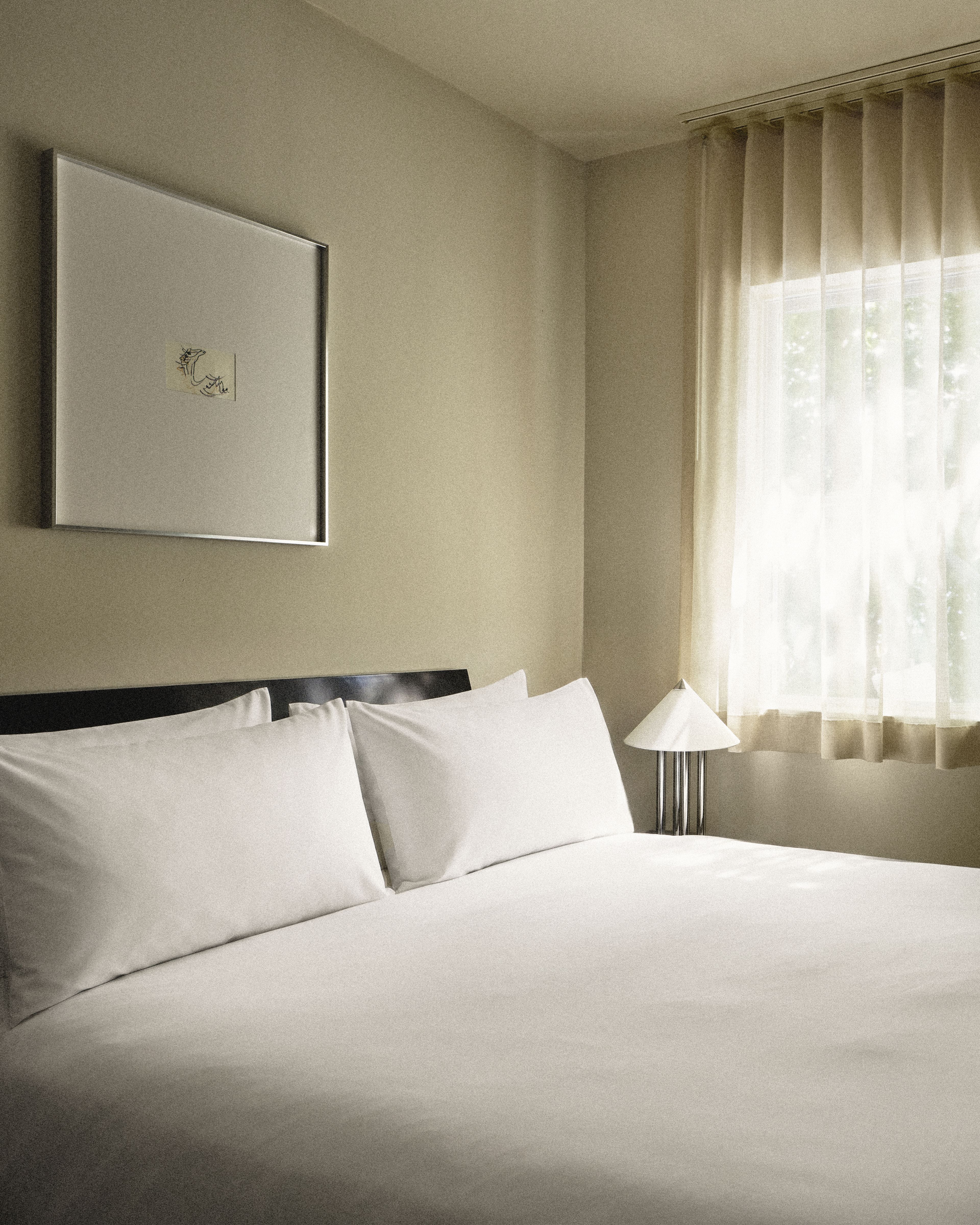 Bed with crisp white linens, bedside lamp, and contemporary artwork in a bright Perroquet Hotel guest room.