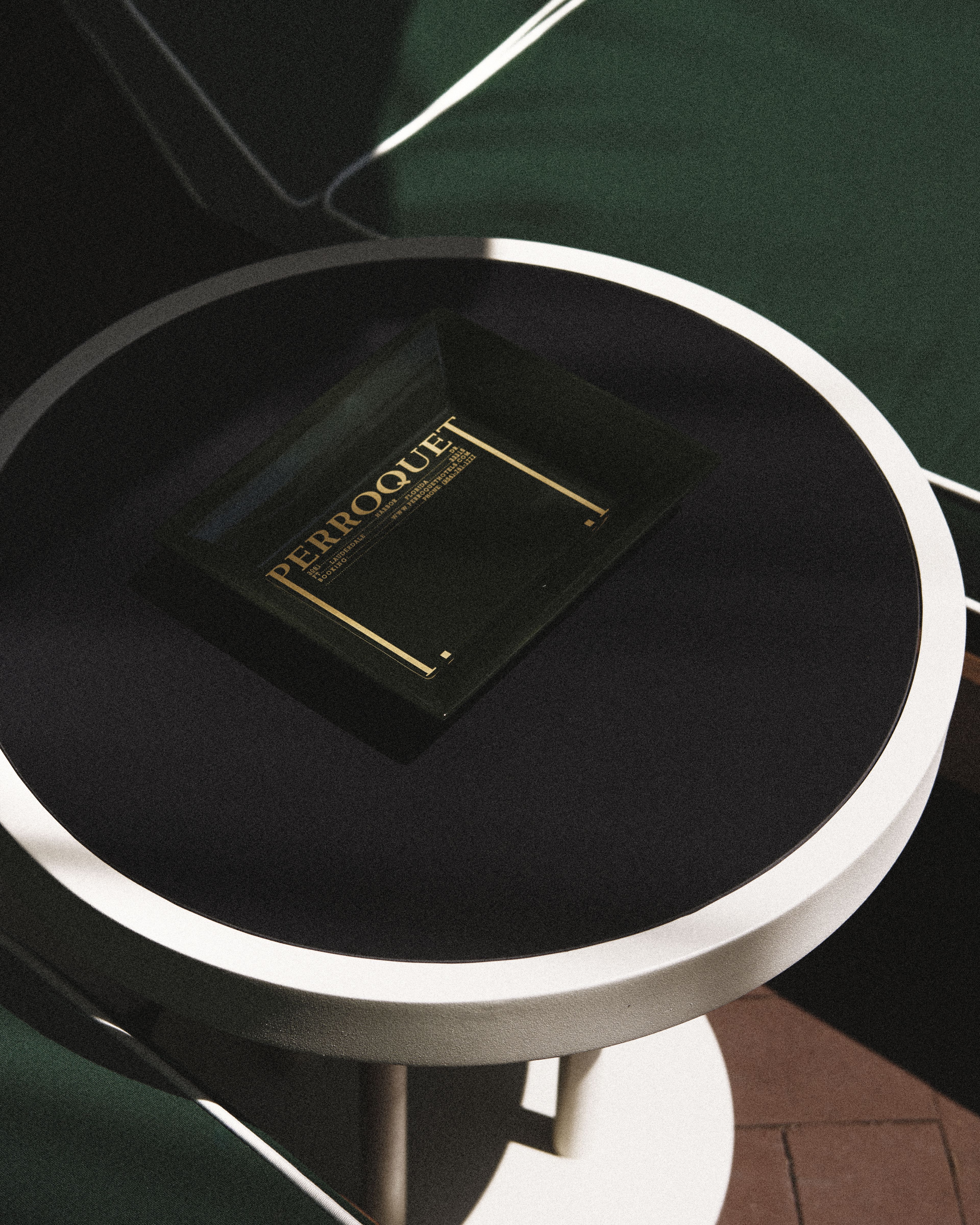 Perroquet Hotel branded welcome tray displayed on a modern round side table in the courtyard.