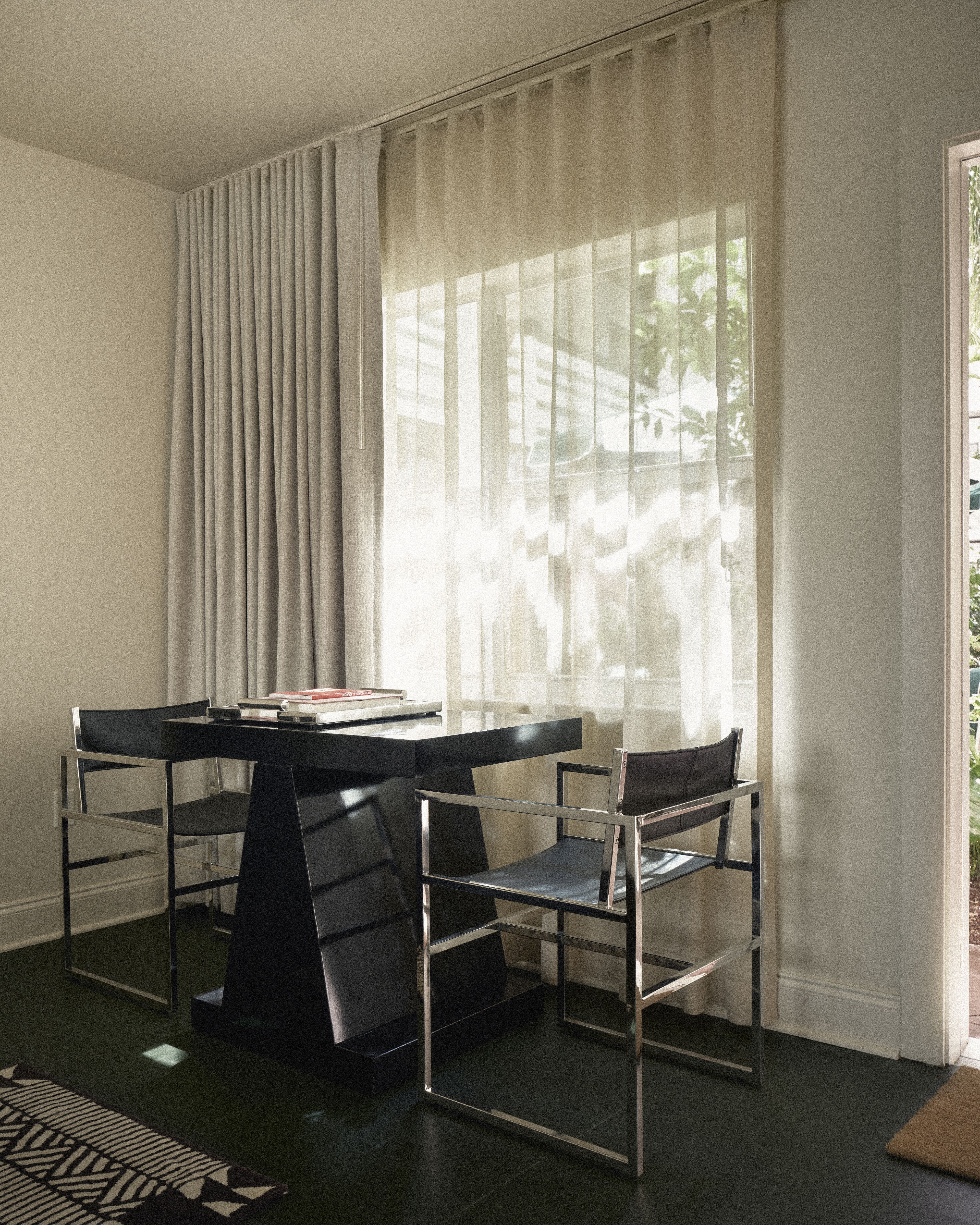 In-room dining table with contemporary chairs beside floor-to-ceiling sheer curtains in a Perroquet Hotel suite.