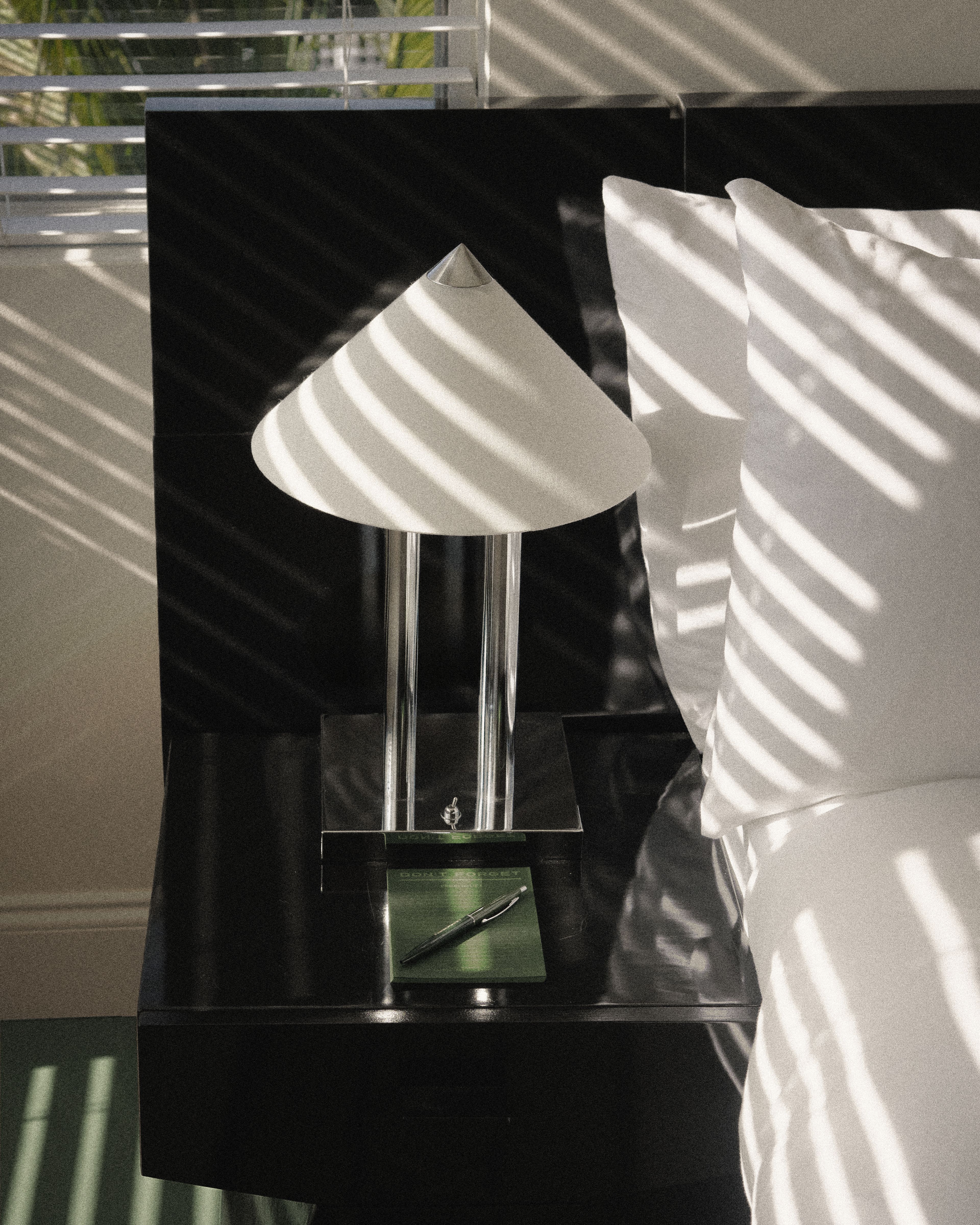Modern bedside table with sculptural lamp, notebook, and crisp white bedding in a guest room at Perroquet Hotel.