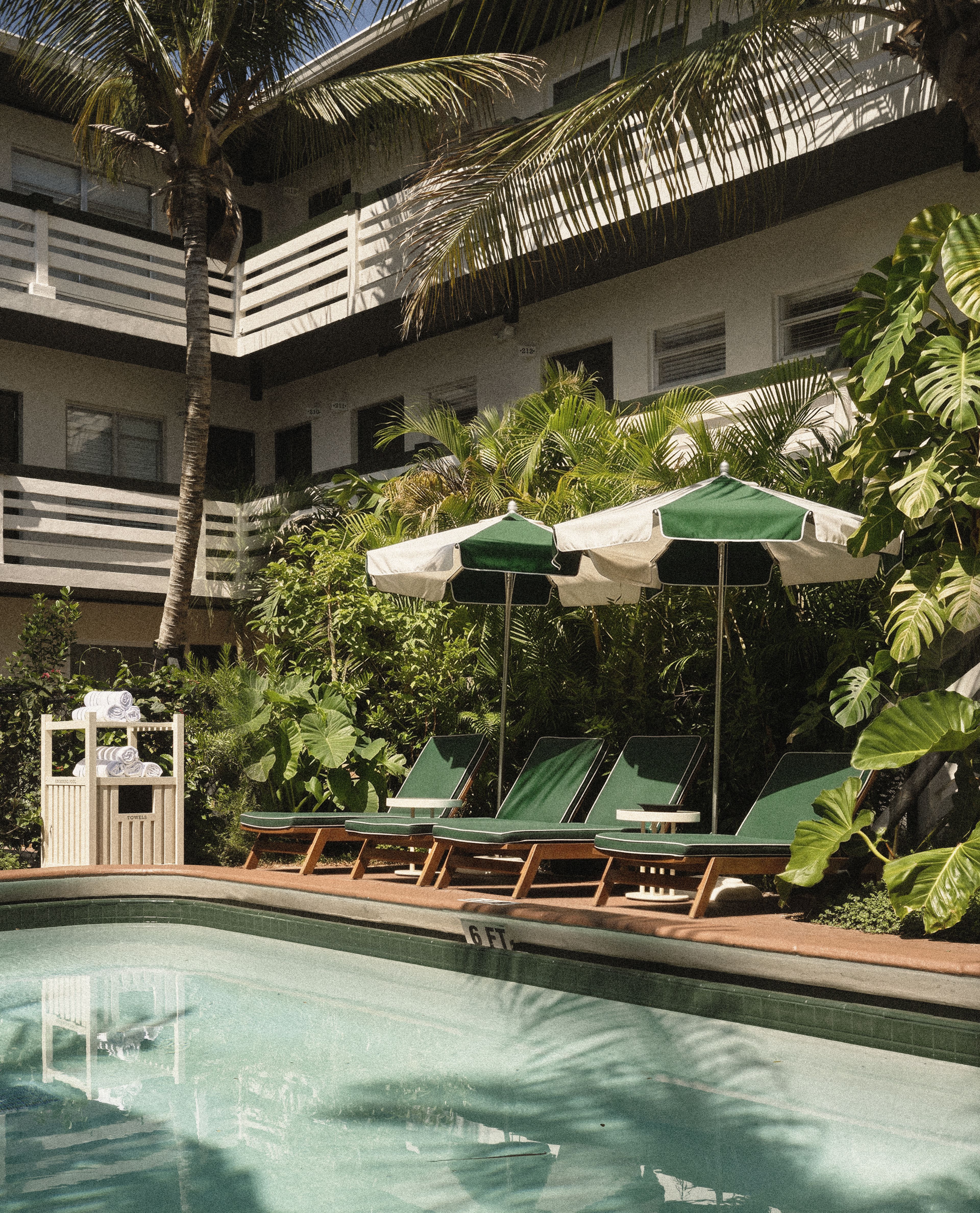 Palm-lined swimming pool surrounded by tropical gardens and green lounge chairs at Perroquet Hotel.