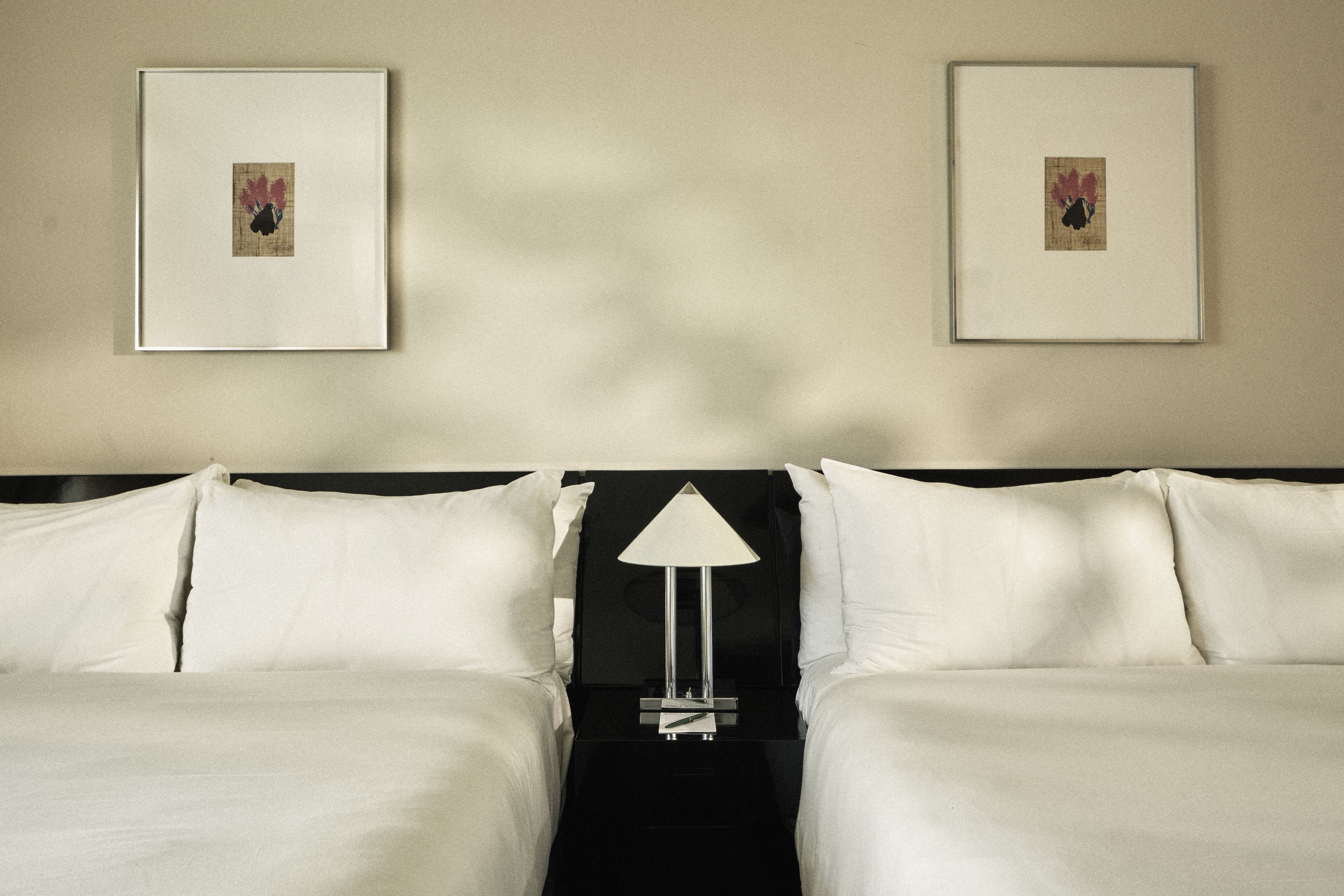 Two queen beds with crisp white linens, sculptural bedside lamp, and contemporary artwork in a Perroquet Hotel guest room.