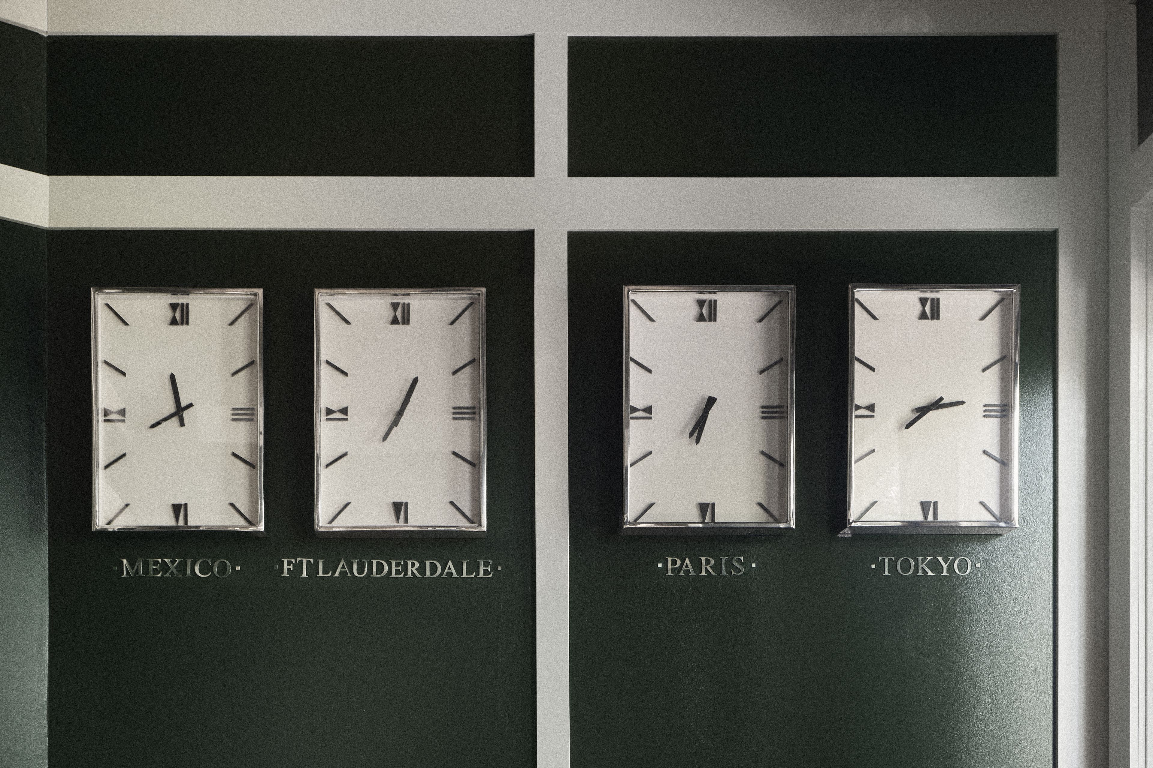 Close-up of custom world clocks in the Perroquet Hotel lobby featuring Fort Lauderdale, Paris, Tokyo, and Mexico.