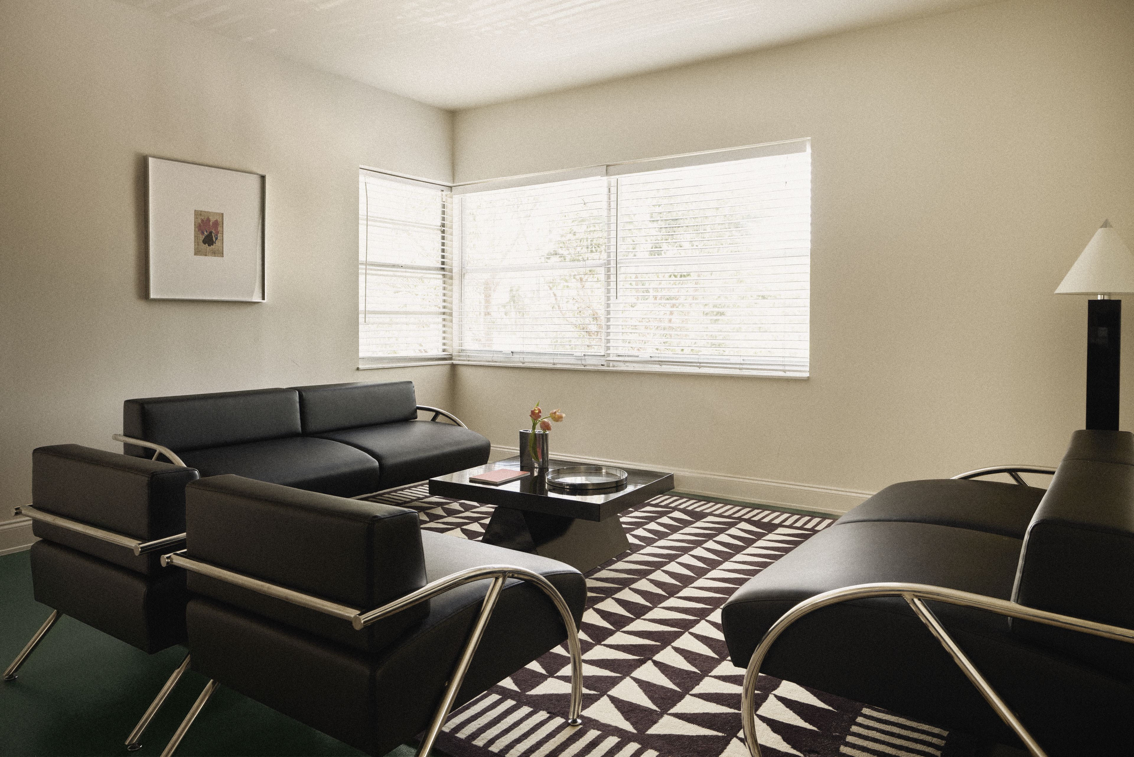 Suite living room with black leather seating, geometric rug, and modern coffee table at Perroquet Hotel.