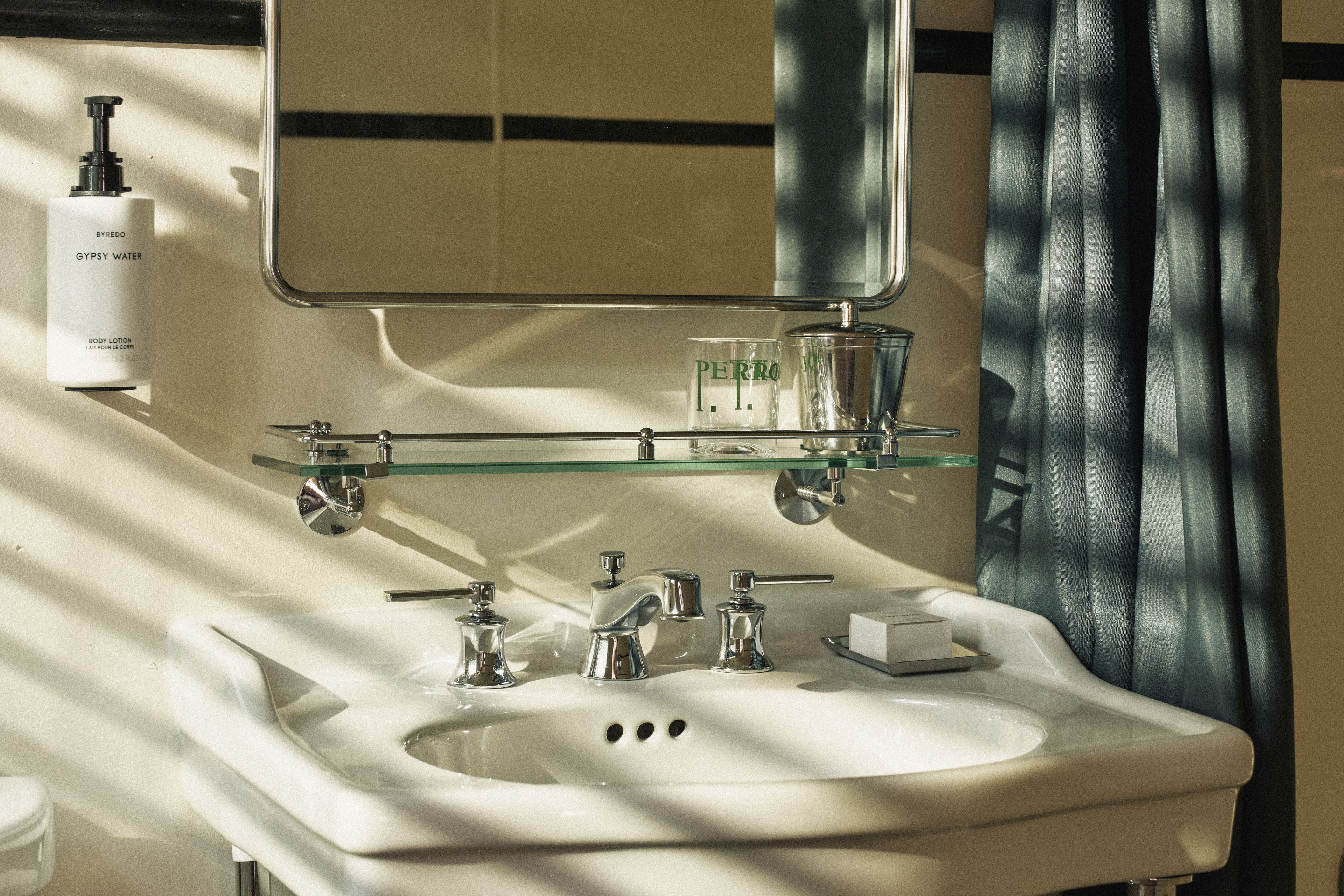 Close-up of the guest bathroom vanity featuring a pedestal sink, chrome fixtures, Byredo toiletries, and Perroquet-branded glassware.